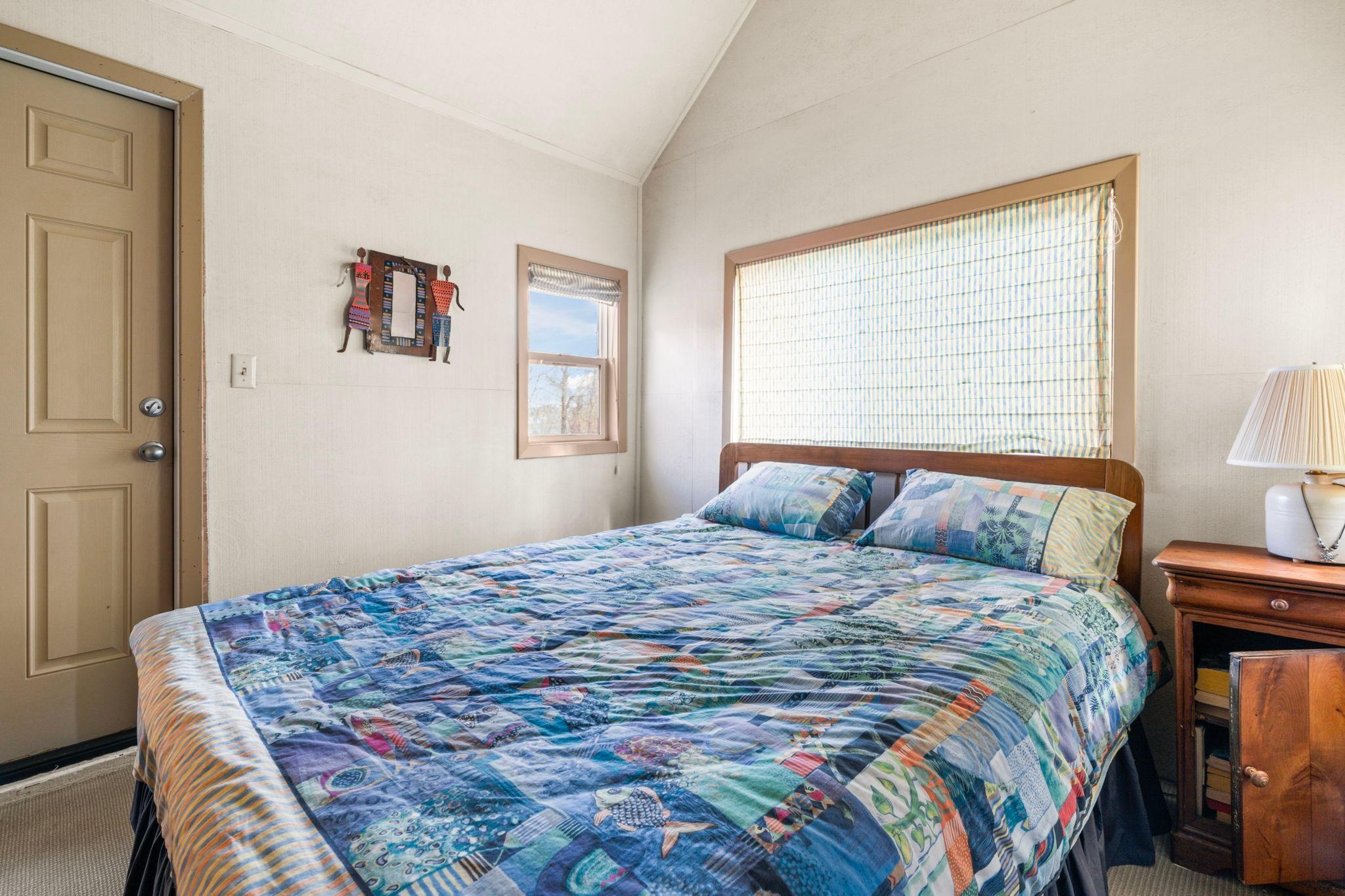 Cozy bedroom in a 1976 custom boathouse with colorful quilt and wooden nightstand.
