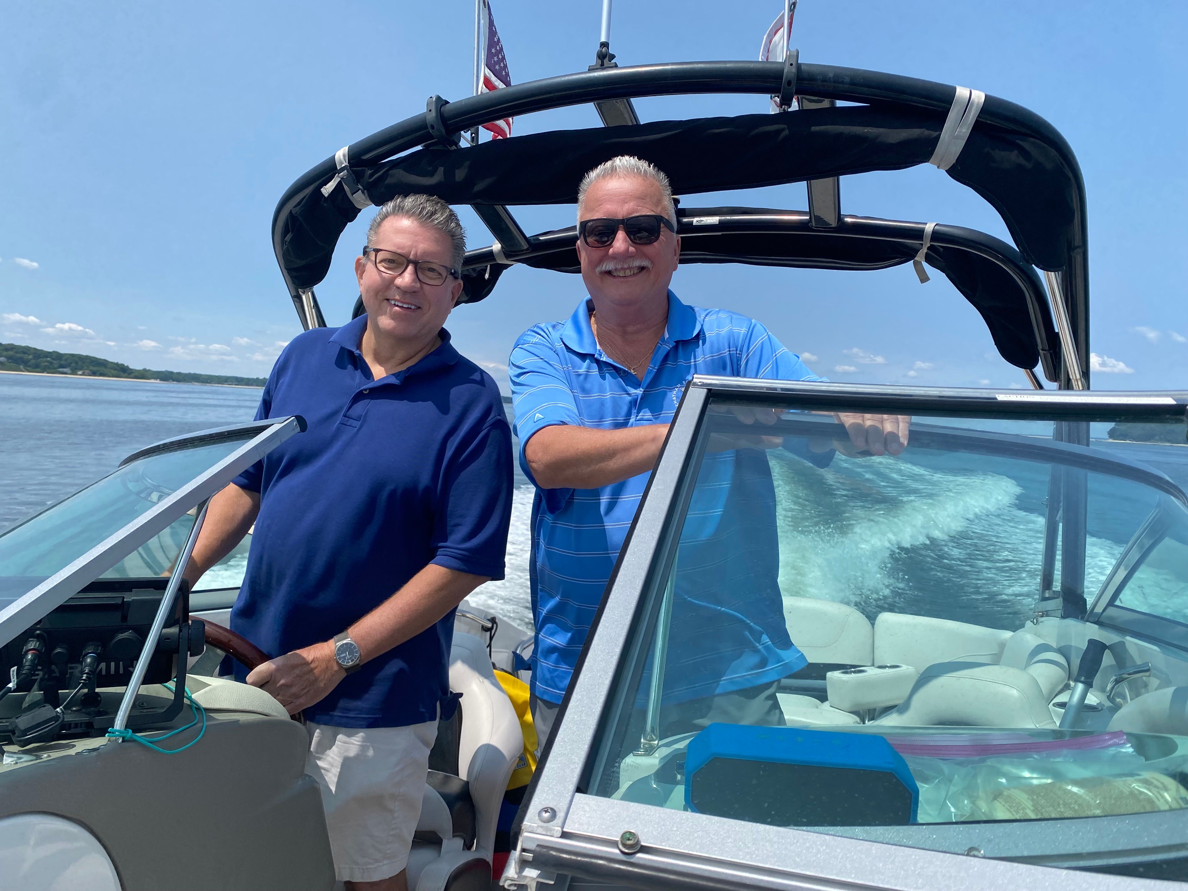 Two men stand on a Crownline E-4 Bowrider boat on the water.