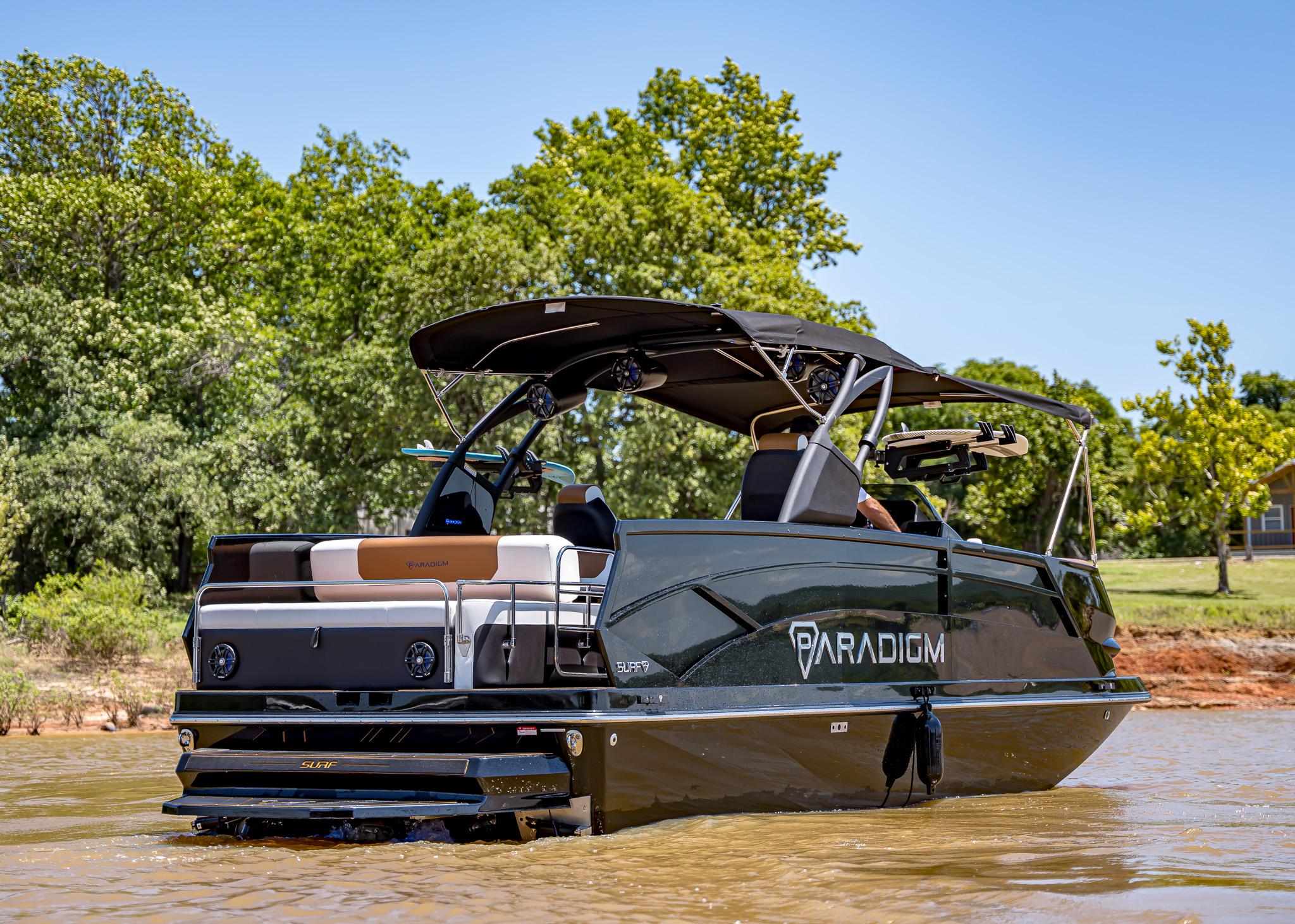 2025 Paradigm 236 boat on water, sleek design, black canopy, lush green background.