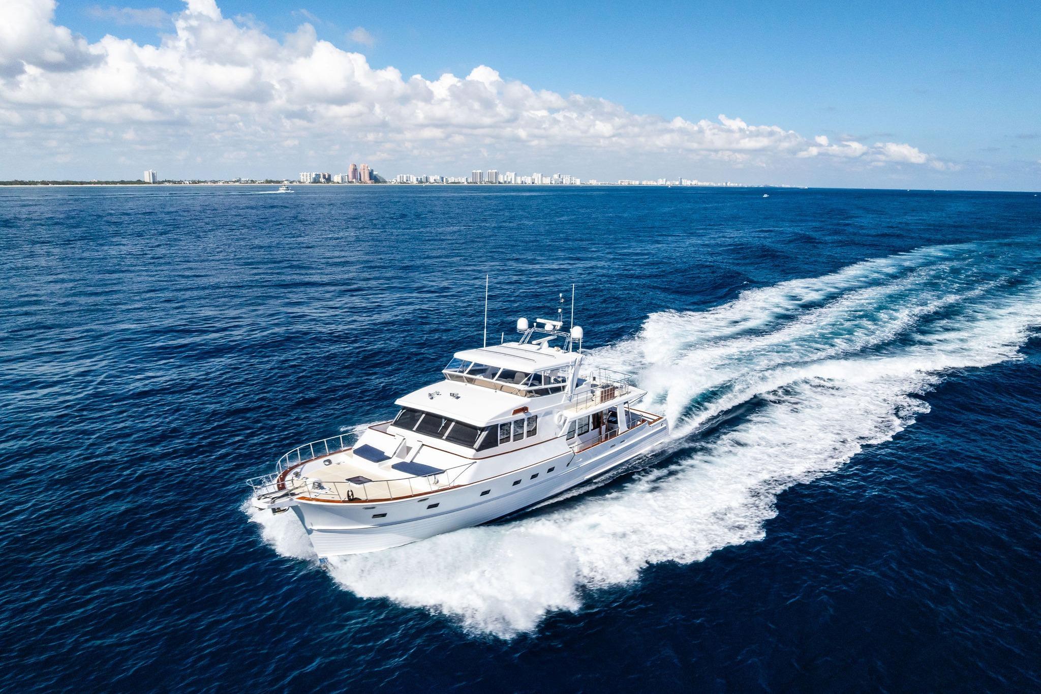 2005 Grand Banks 72 Aleutian RP yacht cruising on open ocean with city skyline in background.