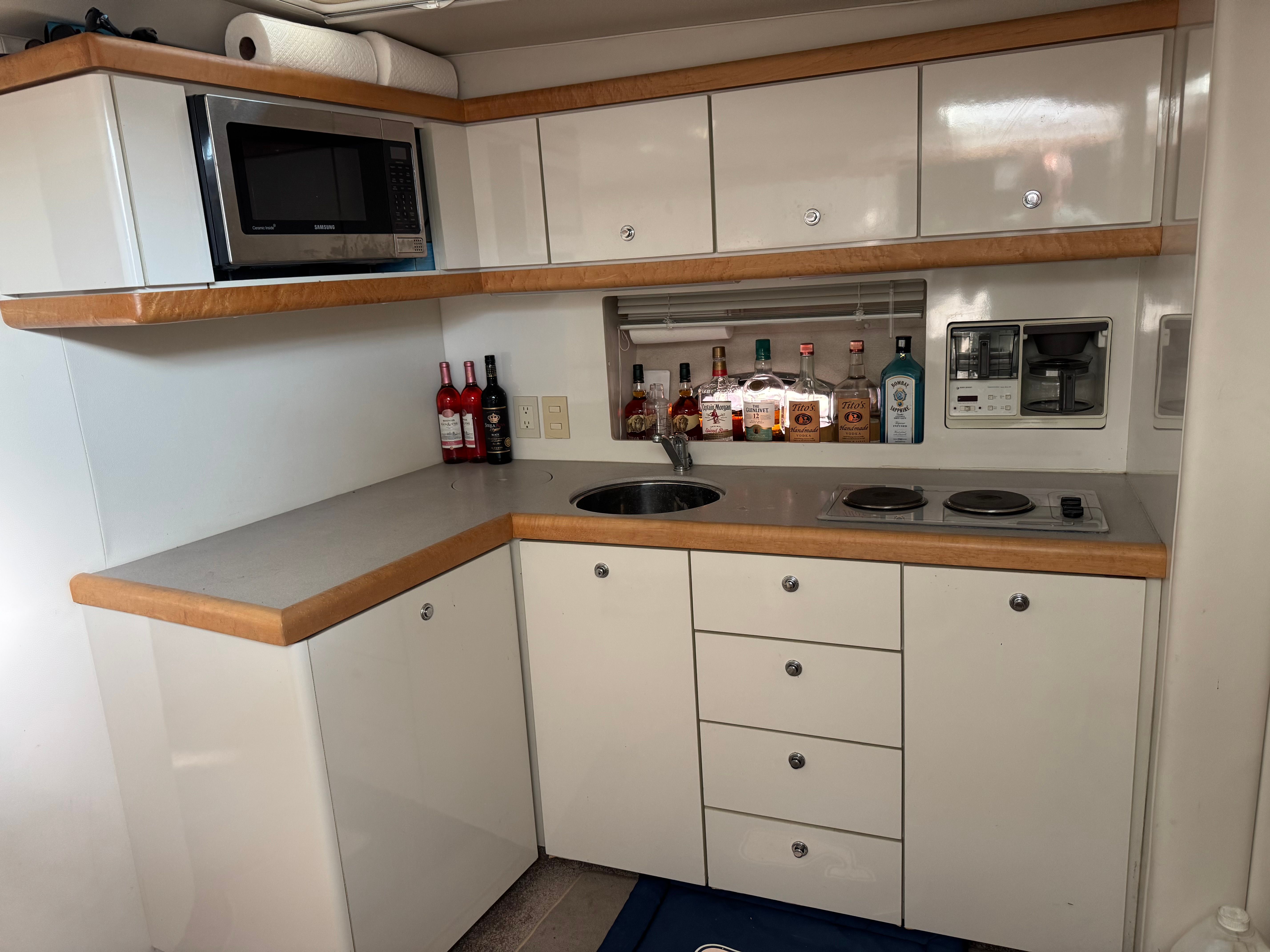 Yacht kitchen area with microwave, stovetop, and bottles of spirits.