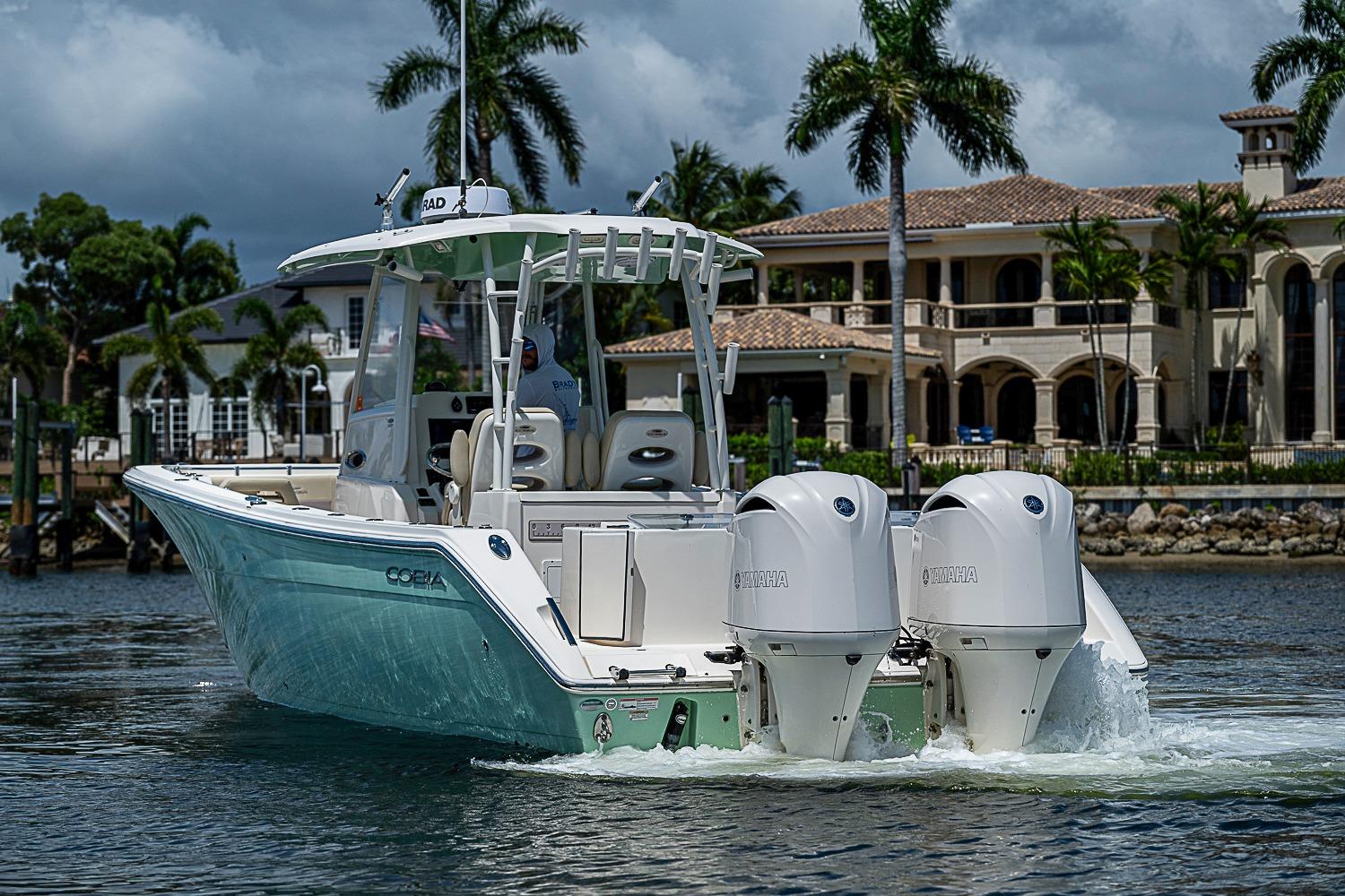 2019 Cobia 320 Center Console boat cruising near luxury waterfront homes.