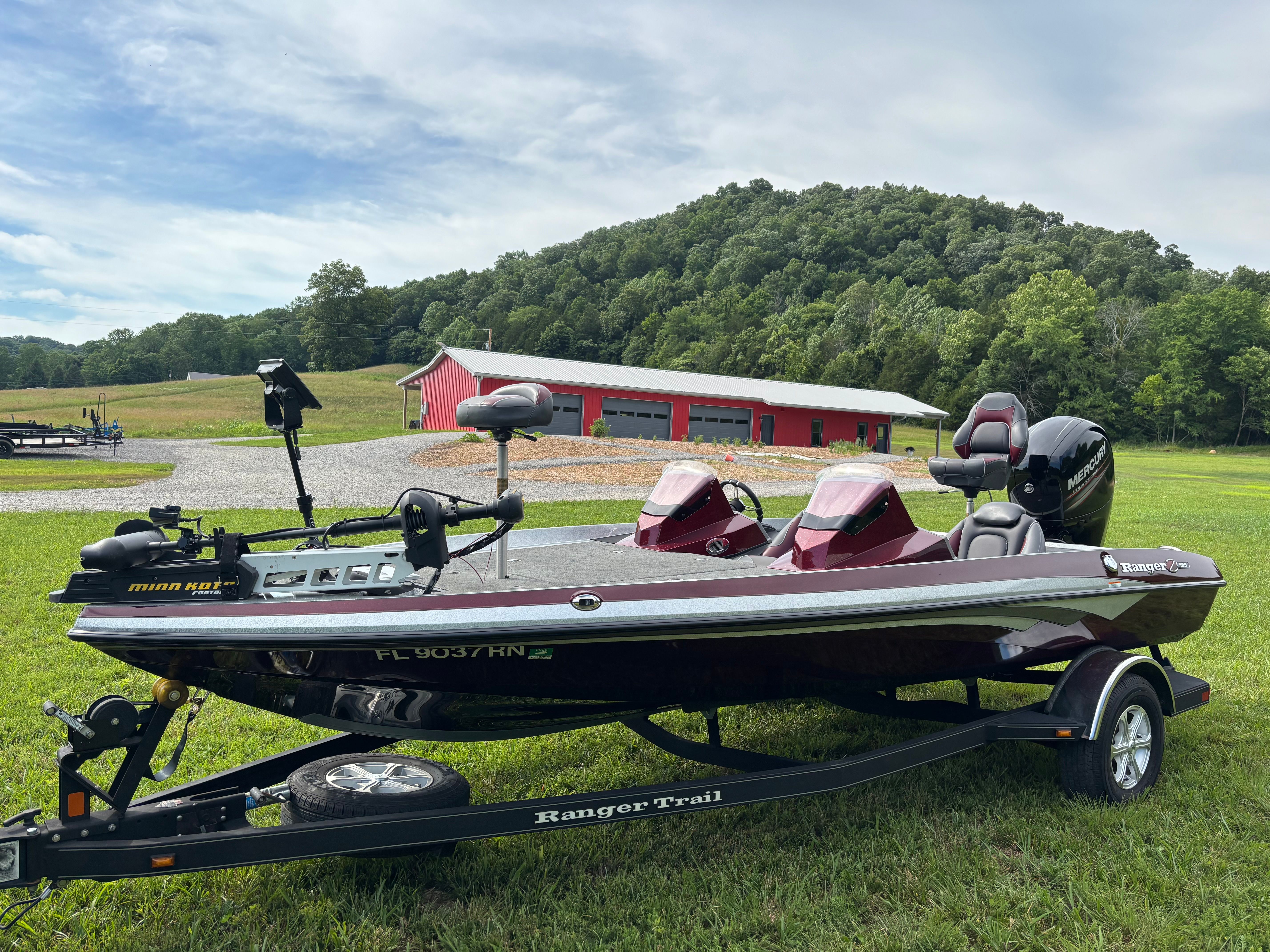 A Ranger Z 185 boat on a trailer in front of a hill with trees.