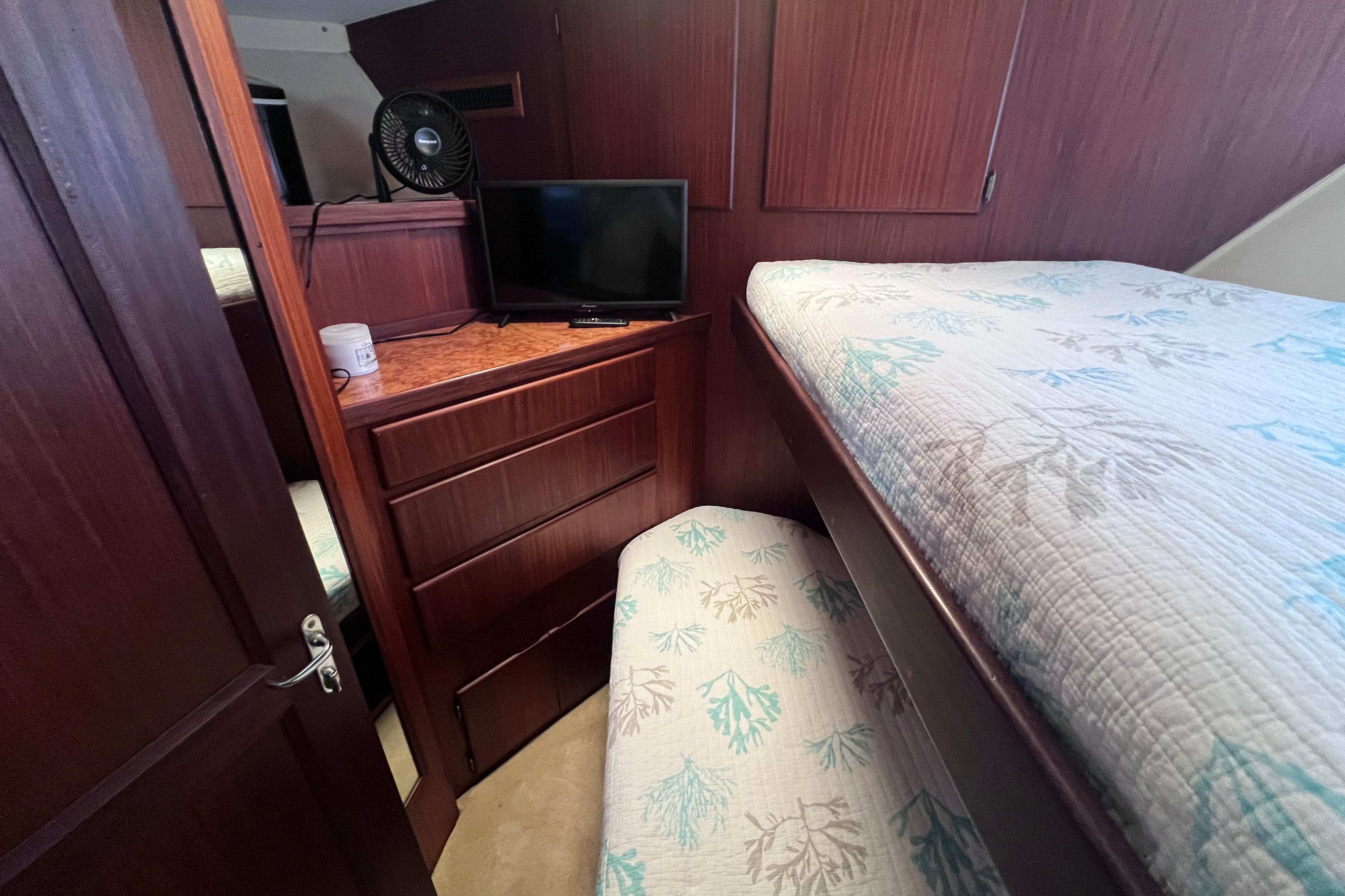 Interior cabin of 1987 Hatteras 70 Cockpit Motor Yacht with bed, TV, and drawers.