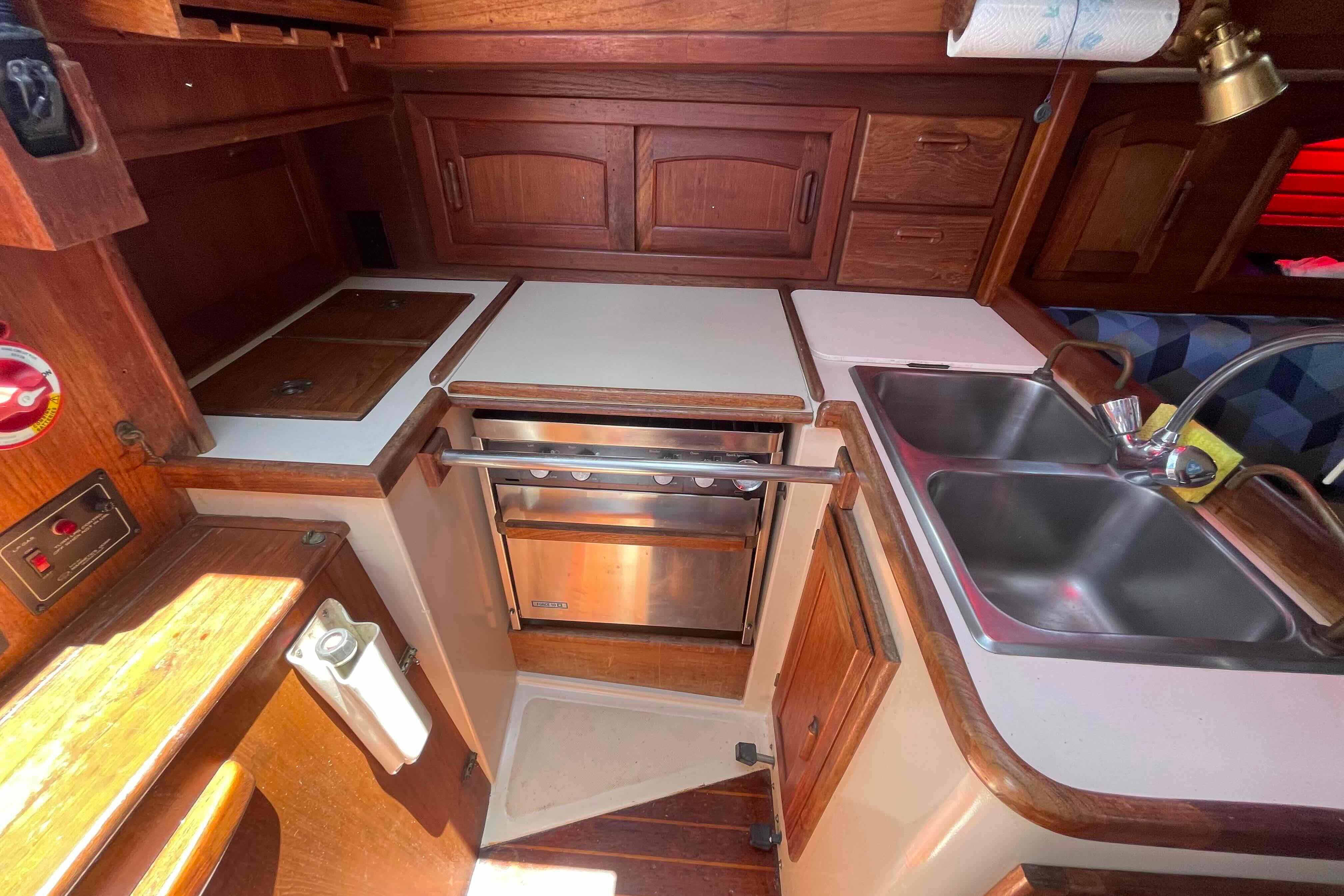 1987 Pacific Seacraft 34 yacht kitchen with wooden cabinetry, dual sink, and compact stove.