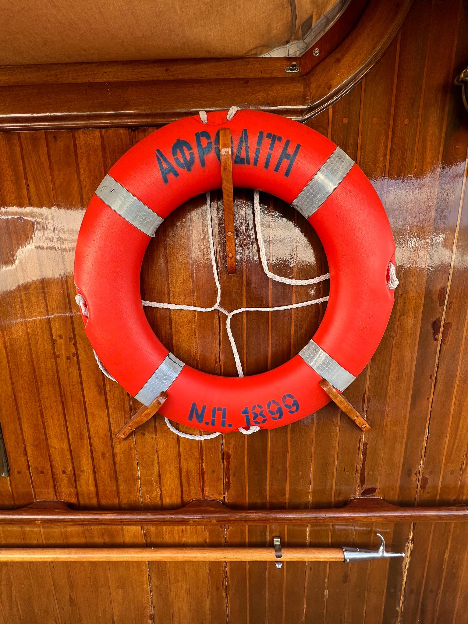 Red lifebuoy on wooden wall, Psarros Shipyard 1969, with Greek text.