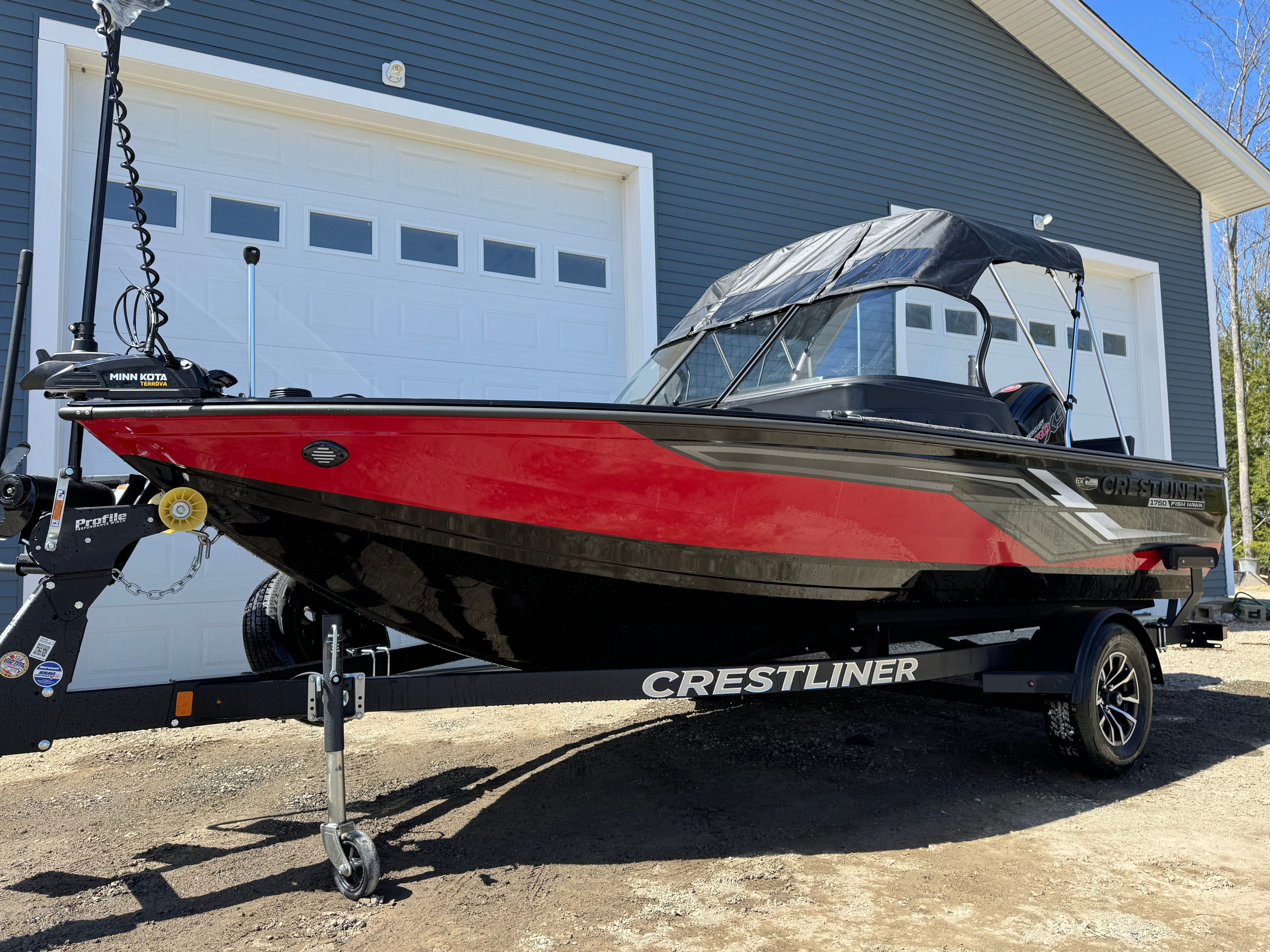 A red Crestliner boat is on a trailer in front of a garage.