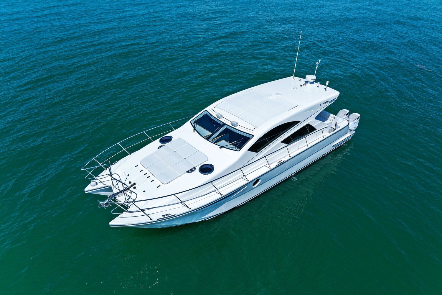 A white catamaran with two hulls sails on calm, blue water.