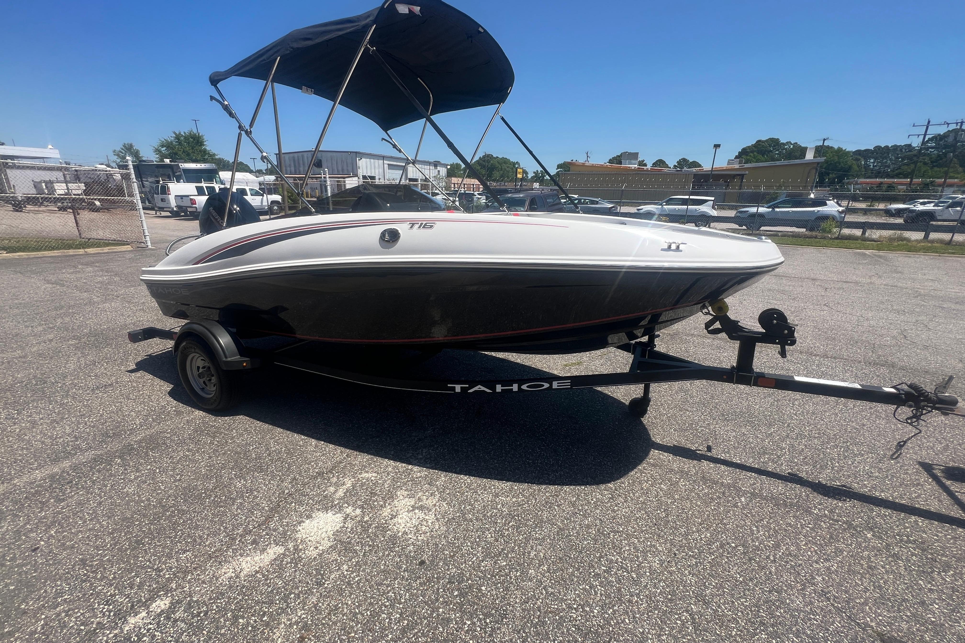 2023 Tahoe T16 boat on trailer with canopy, parked in a lot under clear blue sky.