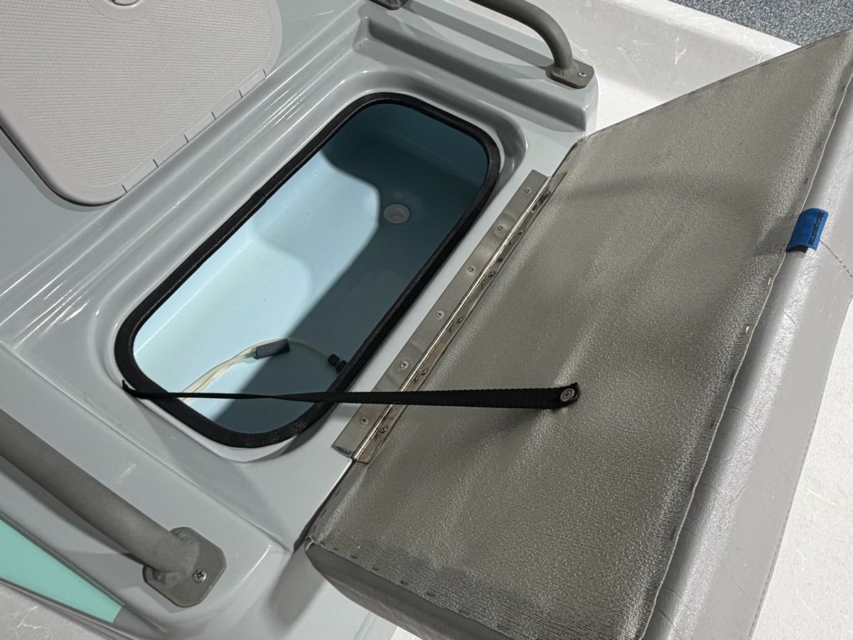 An open storage compartment on a boat with a gray lid and blue interior.