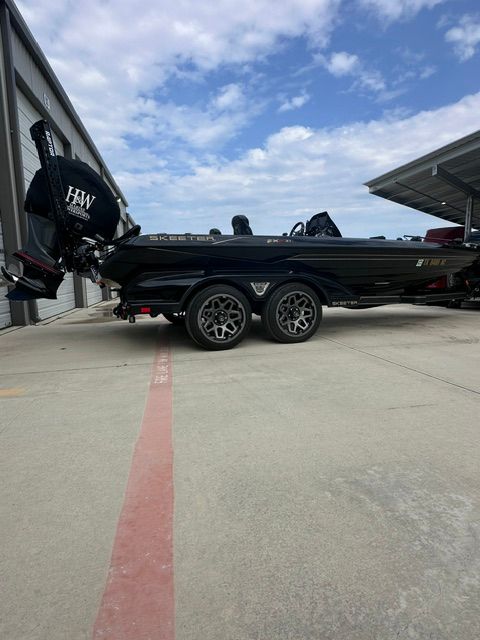 A black Skeeter FXR21 Apex boat on a trailer beside a building.