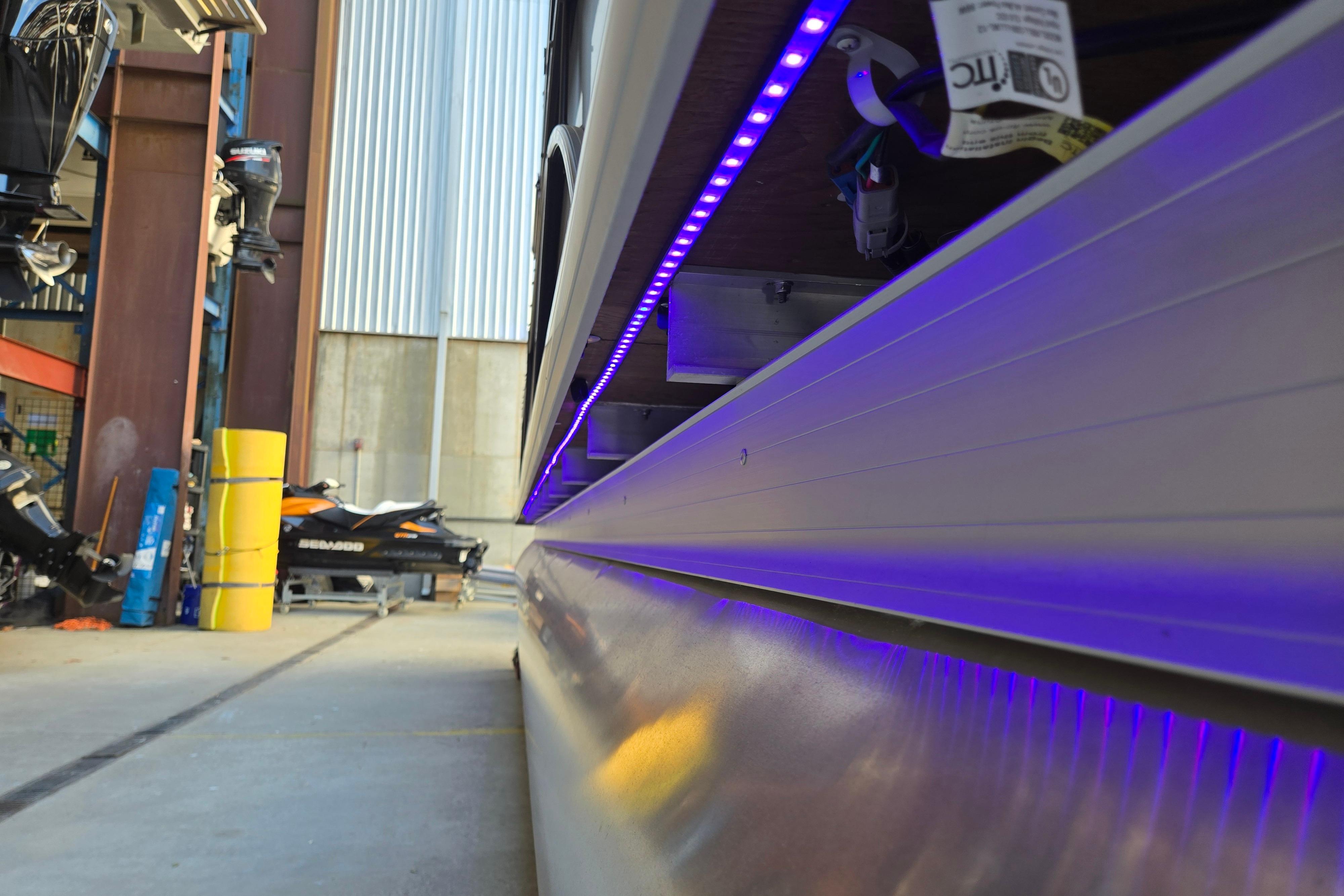2024 Godfrey Sweetwater 2486 SB pontoon with blue LED lights in a marina setting.
