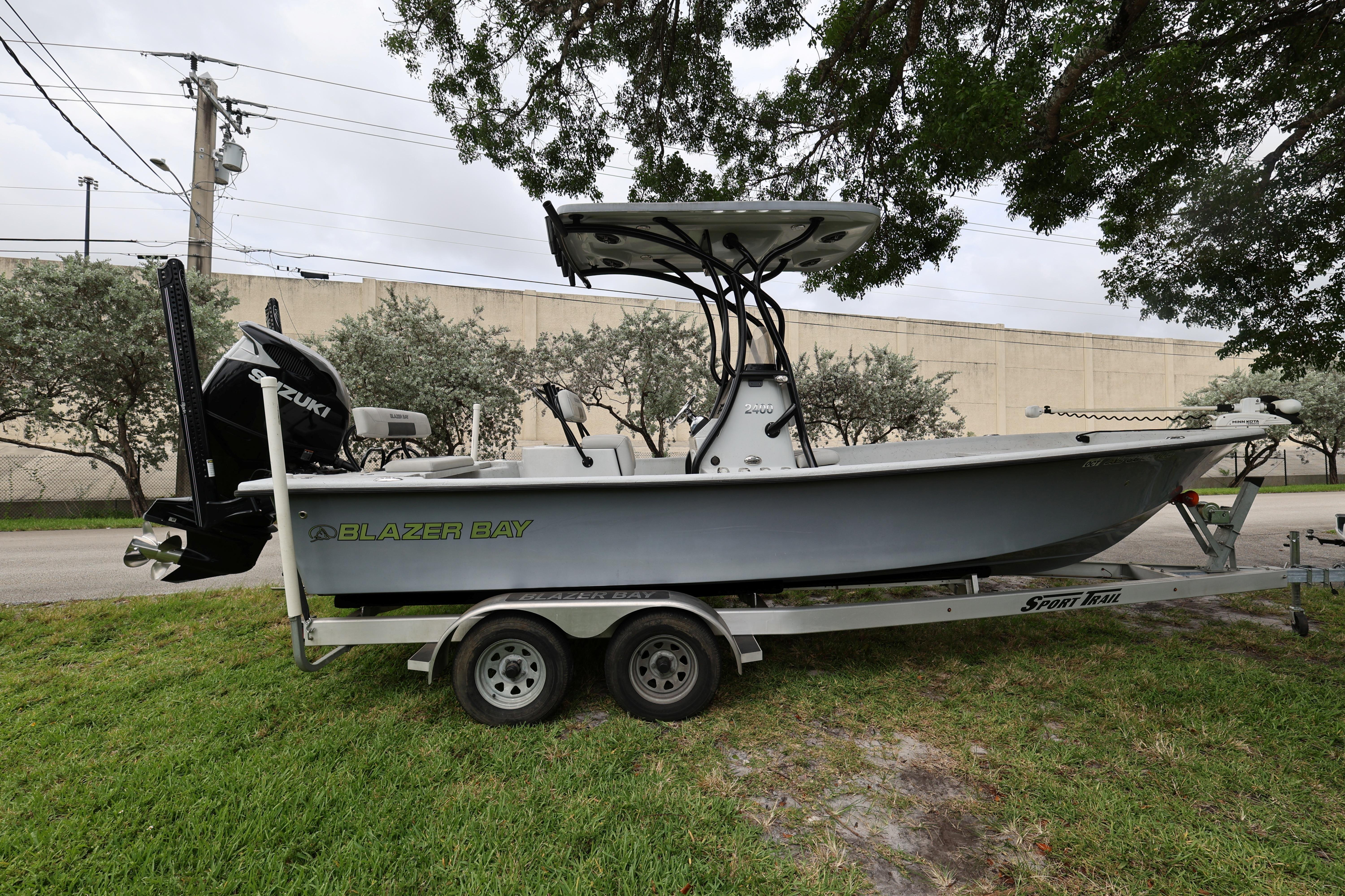 2021 Blazer Bay 2400 boat on trailer, parked on grass under trees.