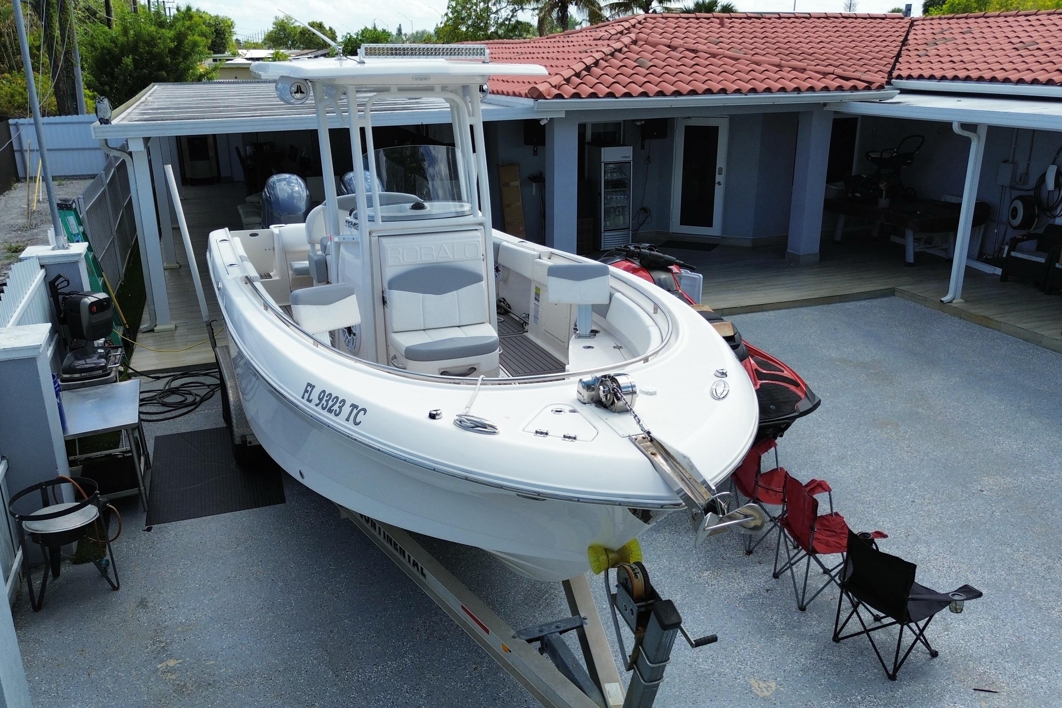 2022 Robalo R242 Center Console boat parked in a driveway with red chairs nearby.