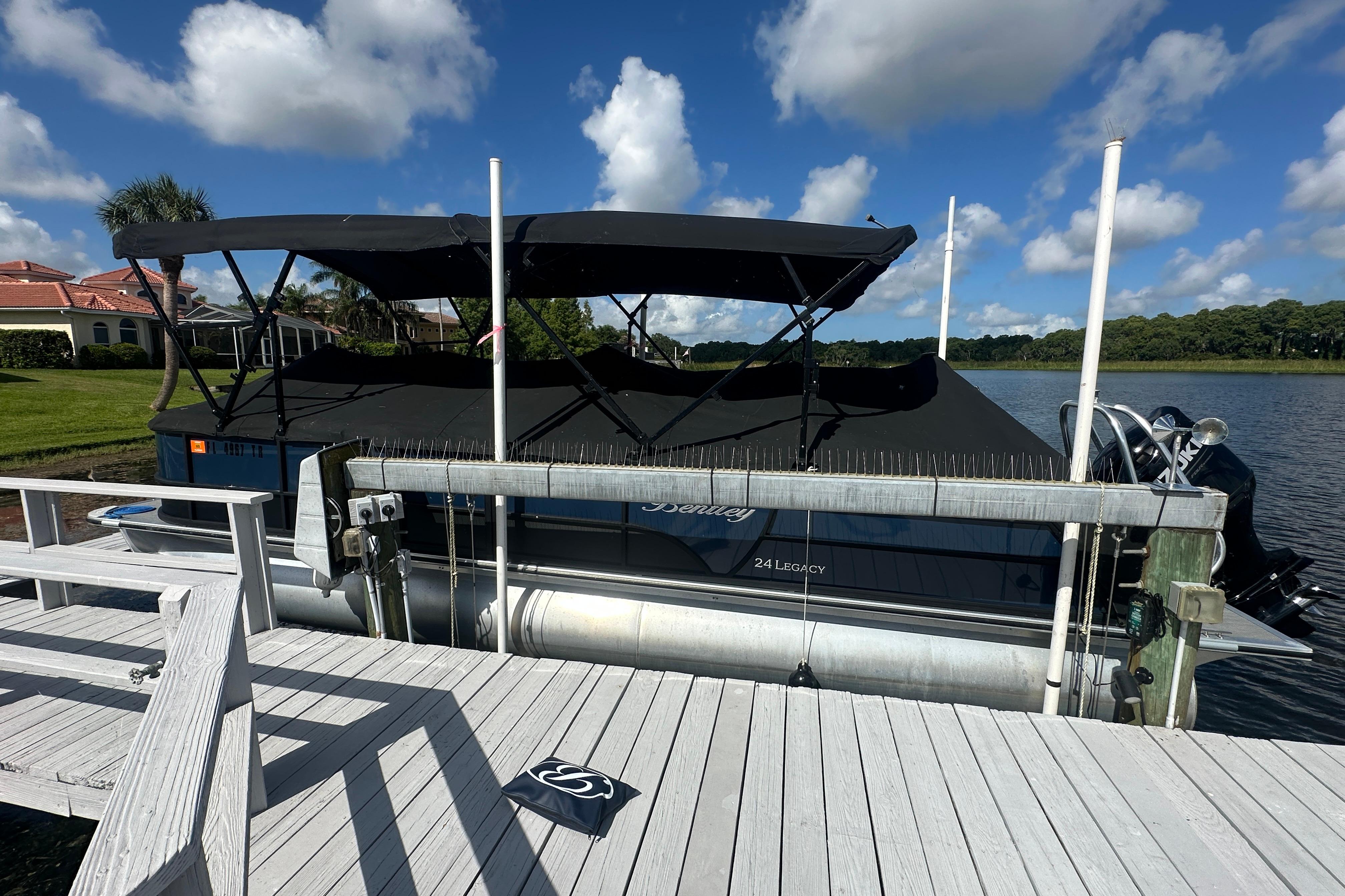 2023 Bentley Pontoons Legacy 243 Swingback docked by a scenic lake under a blue sky.