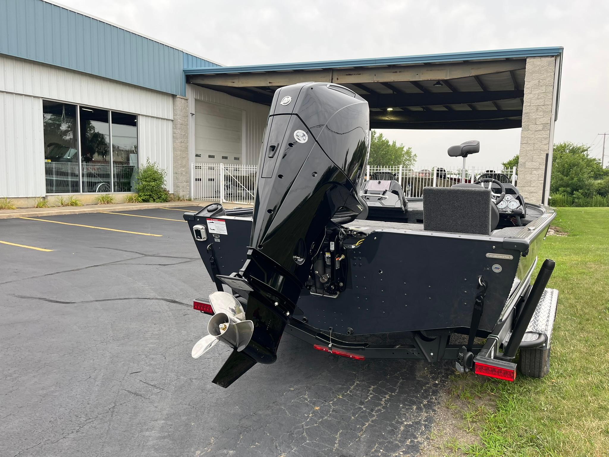 2026 Lund 1875 Pro-V Bass XS boat with powerful outboard motor, parked near a building.