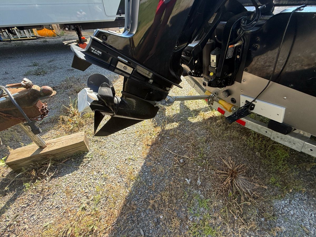 Close-up of a boat's outboard motor on a trailer, surrounded by gravel and grass.