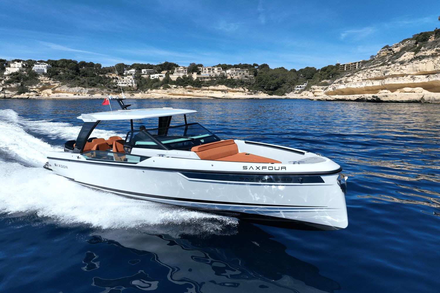A Saxdor SX320 GTO boat speeds on blue water along a rocky coastline.