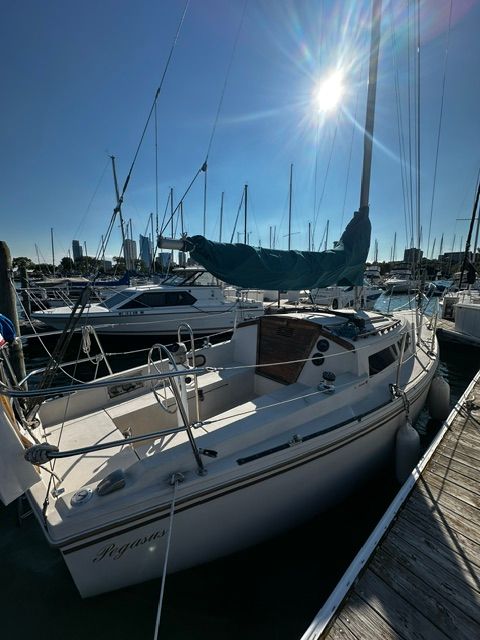 A 1985 Catalina 27 sailboat docked in a marina, surrounded by other boats.