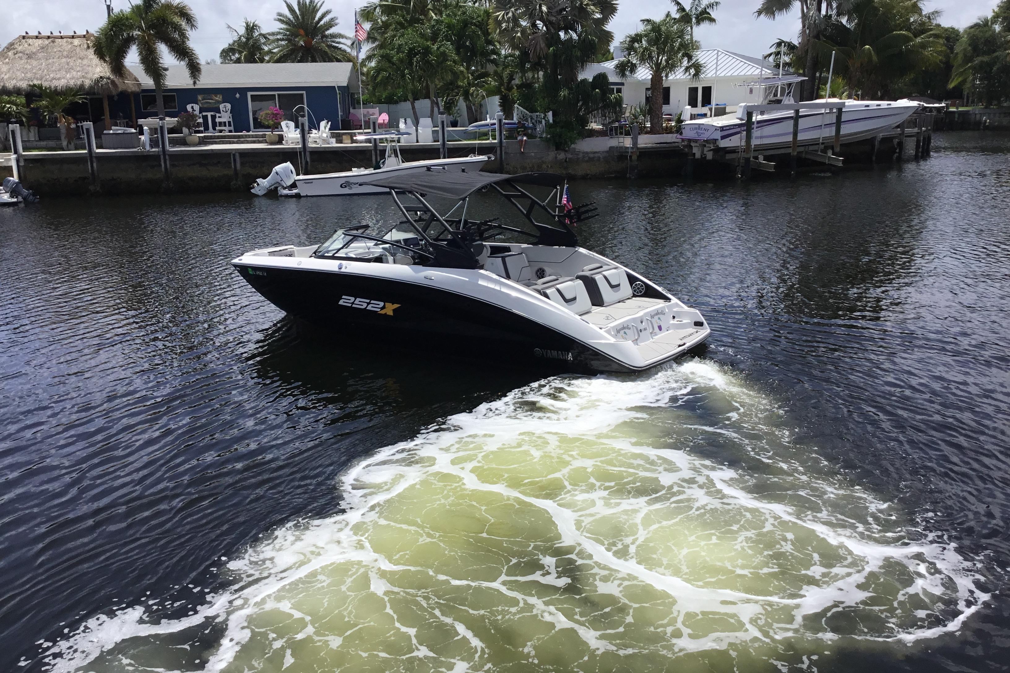 2023 Yamaha Boats 252XE cruising on a scenic waterway with palm trees in the background.