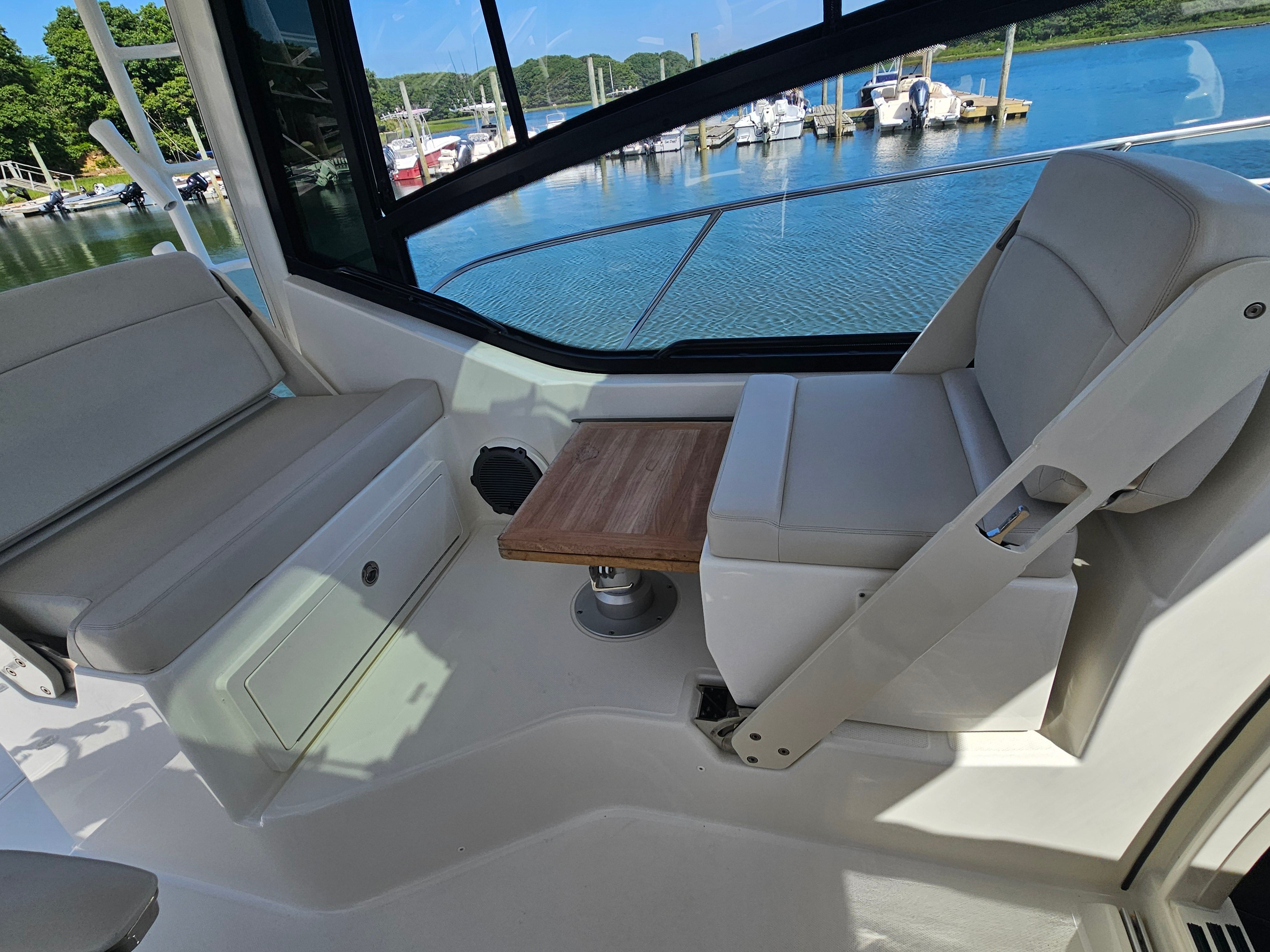 Interior of a Boston Whaler 325 Conquest with seating and a wooden table, docked by the water.