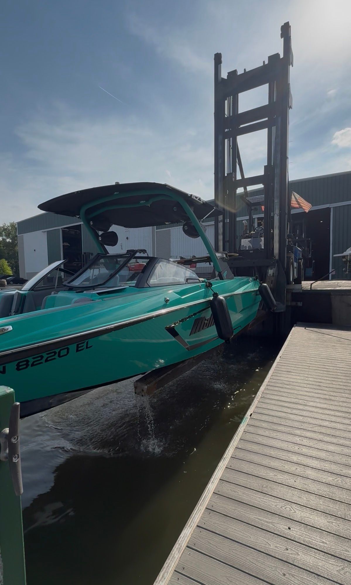 A turquoise Malibu Wakesetter 24 MXZ being lowered into the water by a forklift.