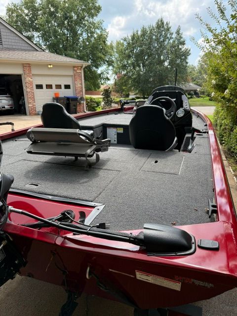 A red 2024 Crestliner XF 179 boat is parked in a driveway. It features two seats and a console.