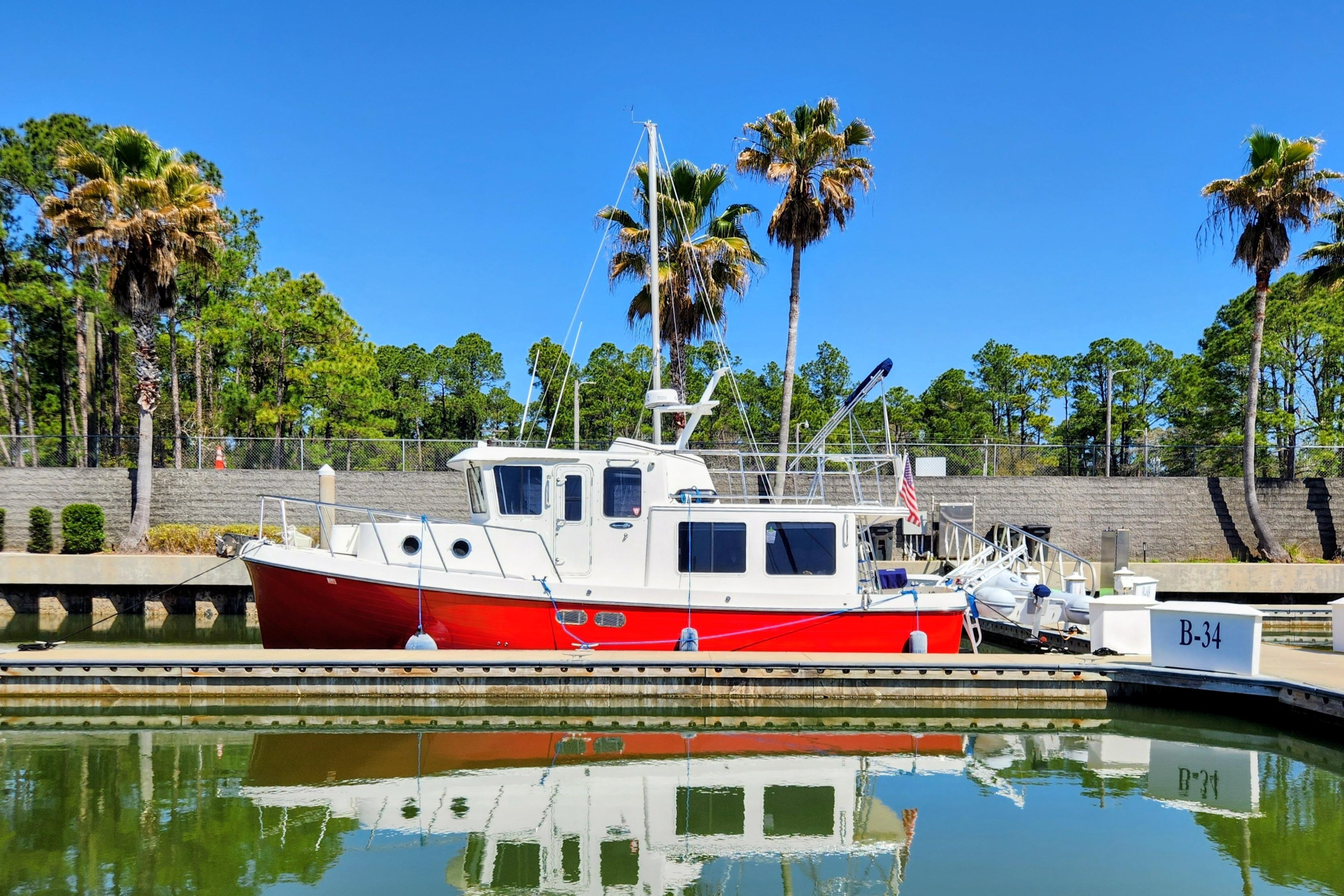 Red and white 2006 American Tug AT docked in a marina with palm trees.