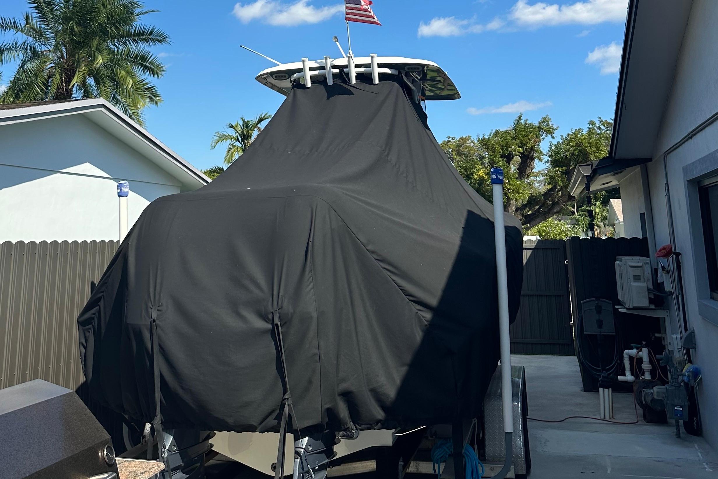 2019 Sea Hunt Gamefish 25 boat covered, parked in driveway with palm trees and blue sky.