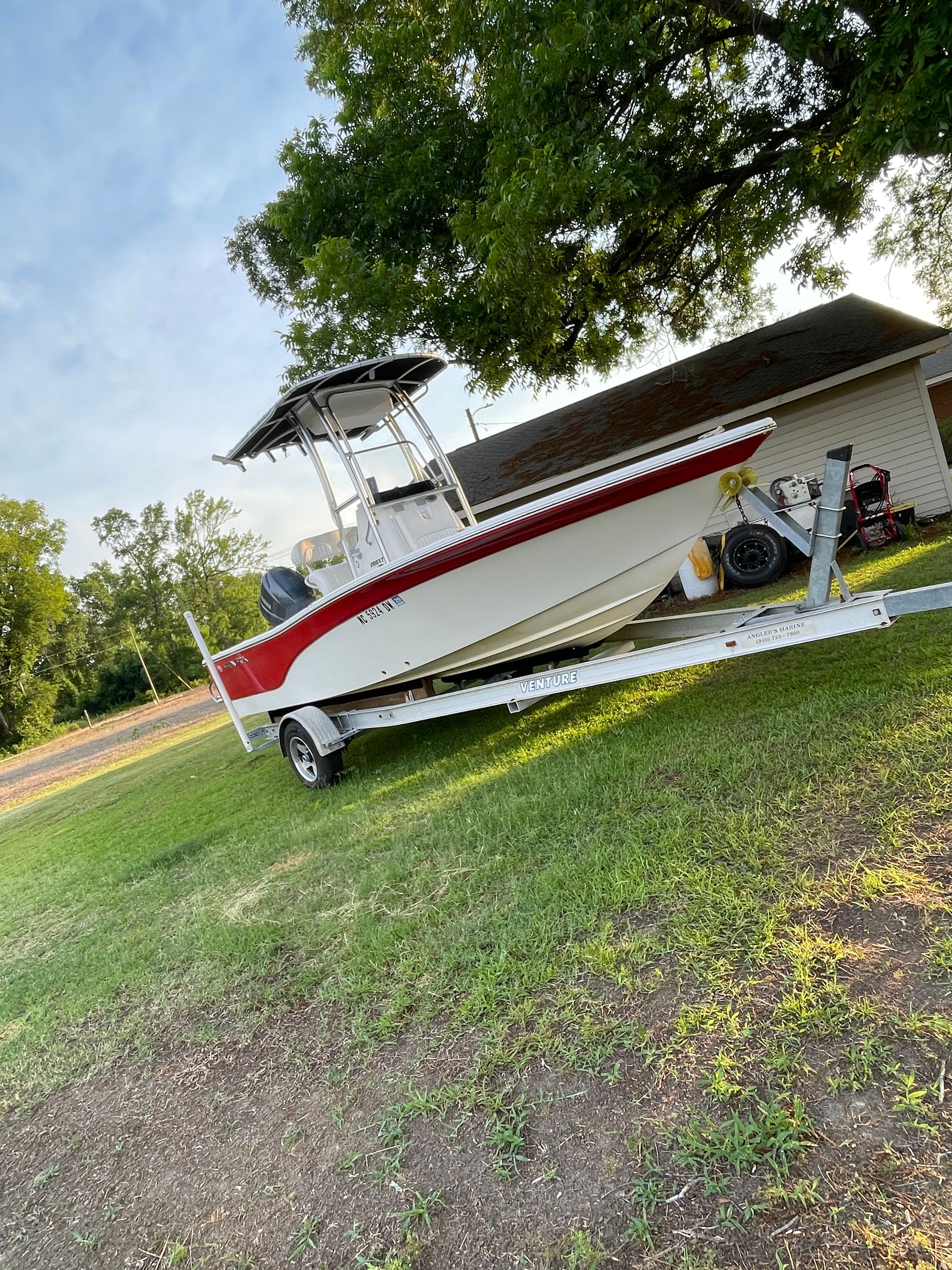 A 2012 Sea Fox 200XT boat on a trailer, parked on grass beside a building.