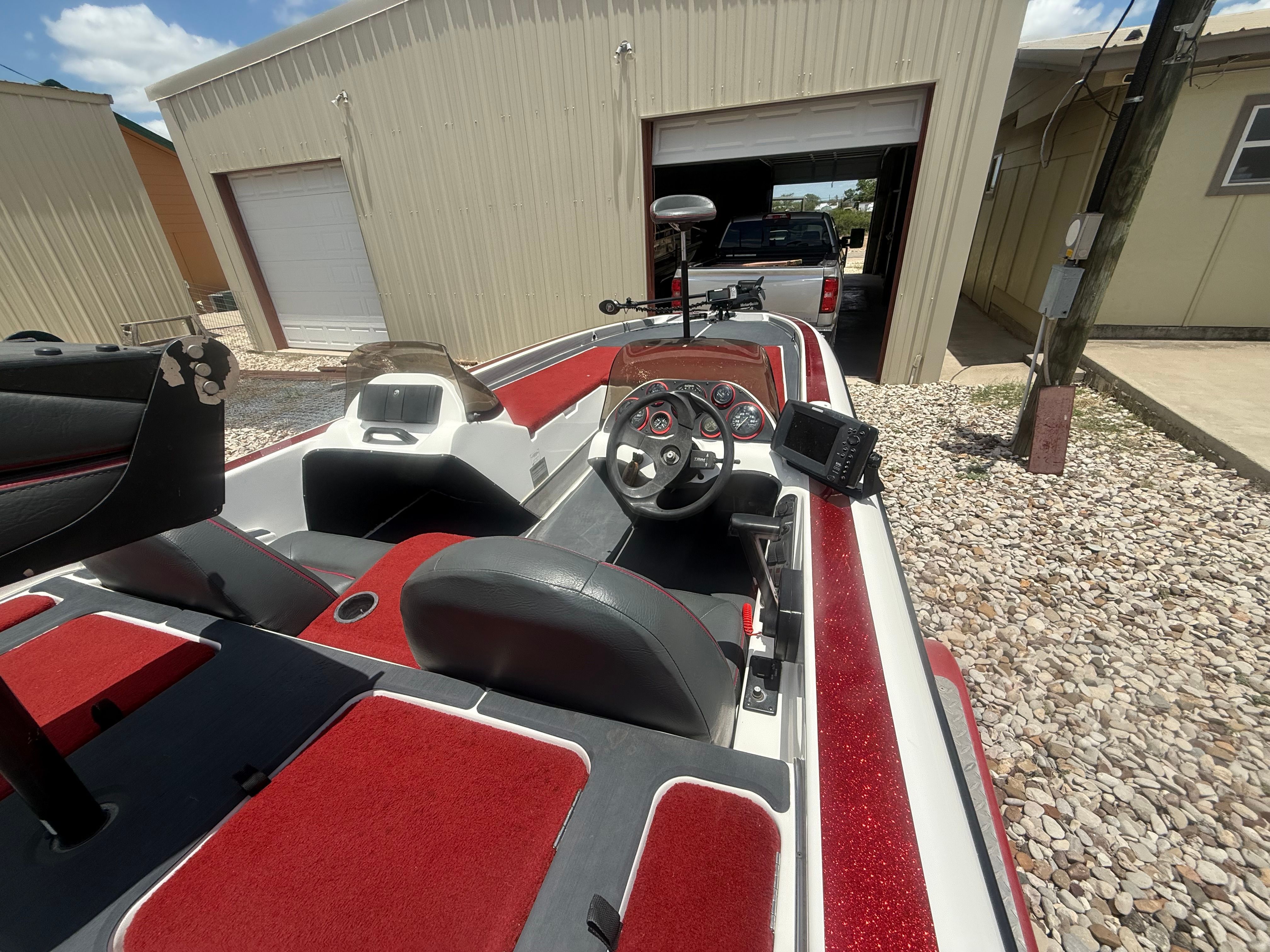 A 1999 Champion 202 boat with red and gray interior, parked in front of a garage.