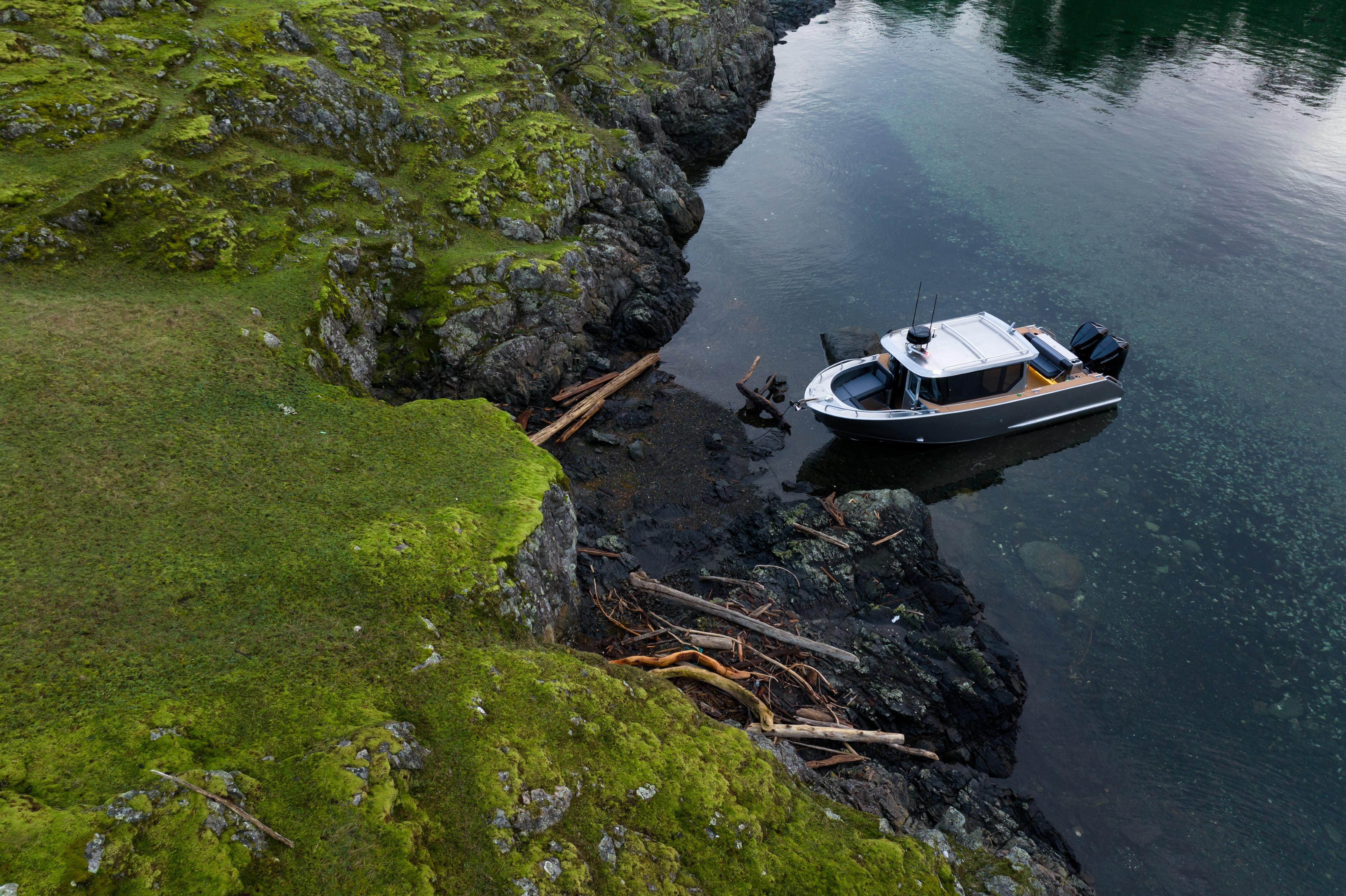 Aerial view of 2026 Jasper Marine Defender 22 moored by rocky, mossy shoreline.