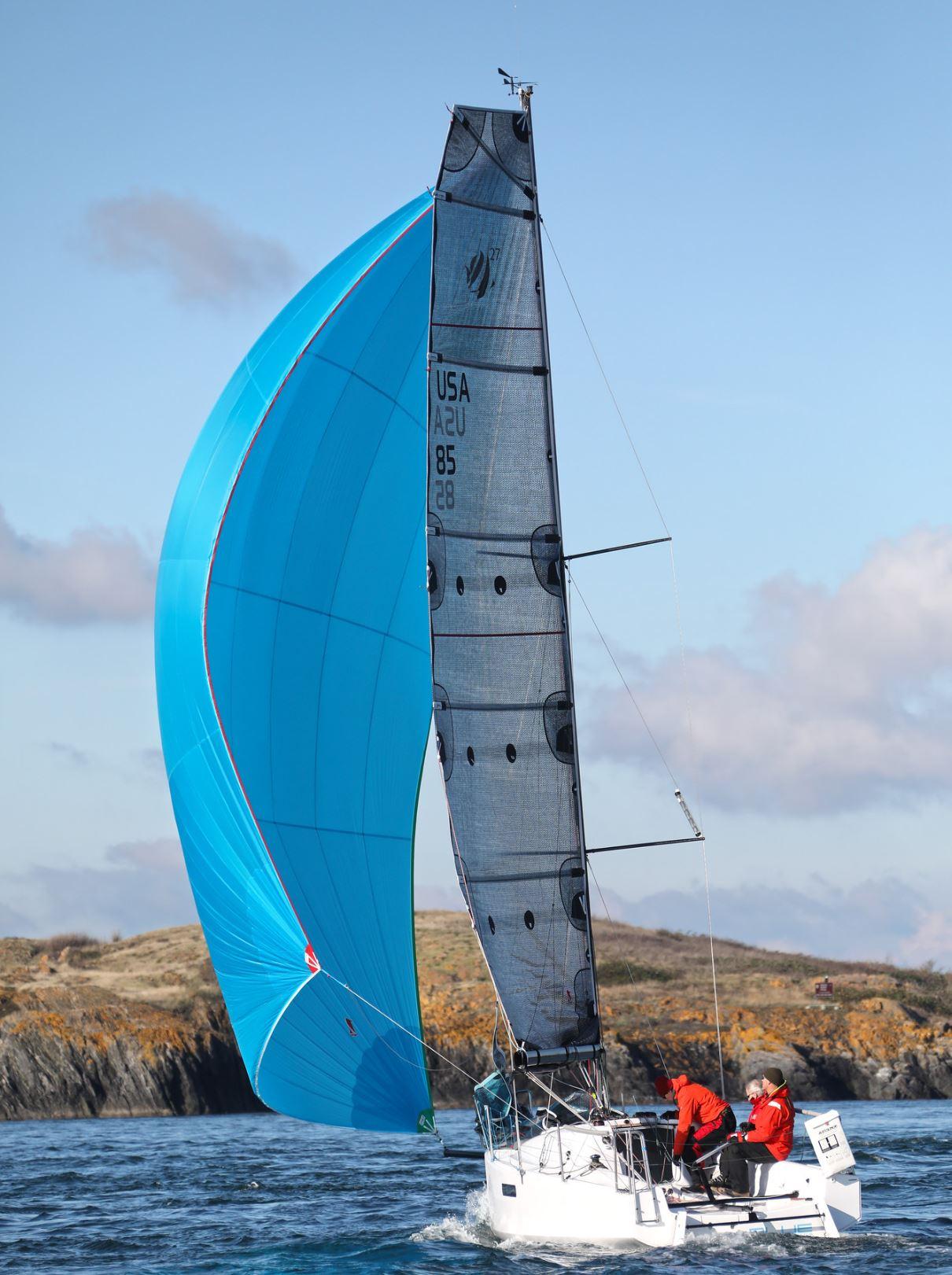 Sailboat Seascape 27, 2018 model, with blue spinnaker sailing near rocky coastline.