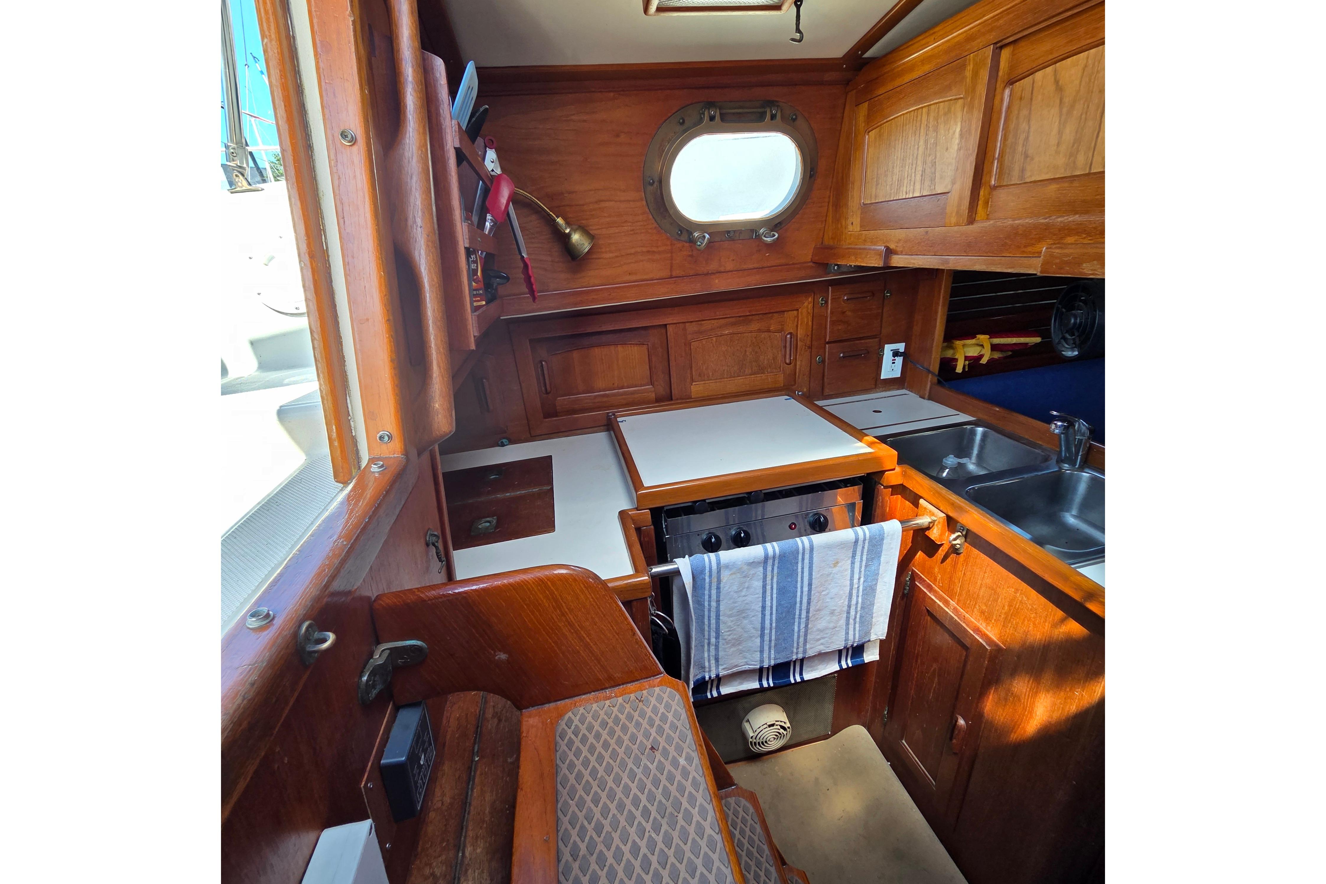 Interior of 1983 Pacific Seacraft 34 sailboat, featuring wooden cabinetry and compact kitchen area.