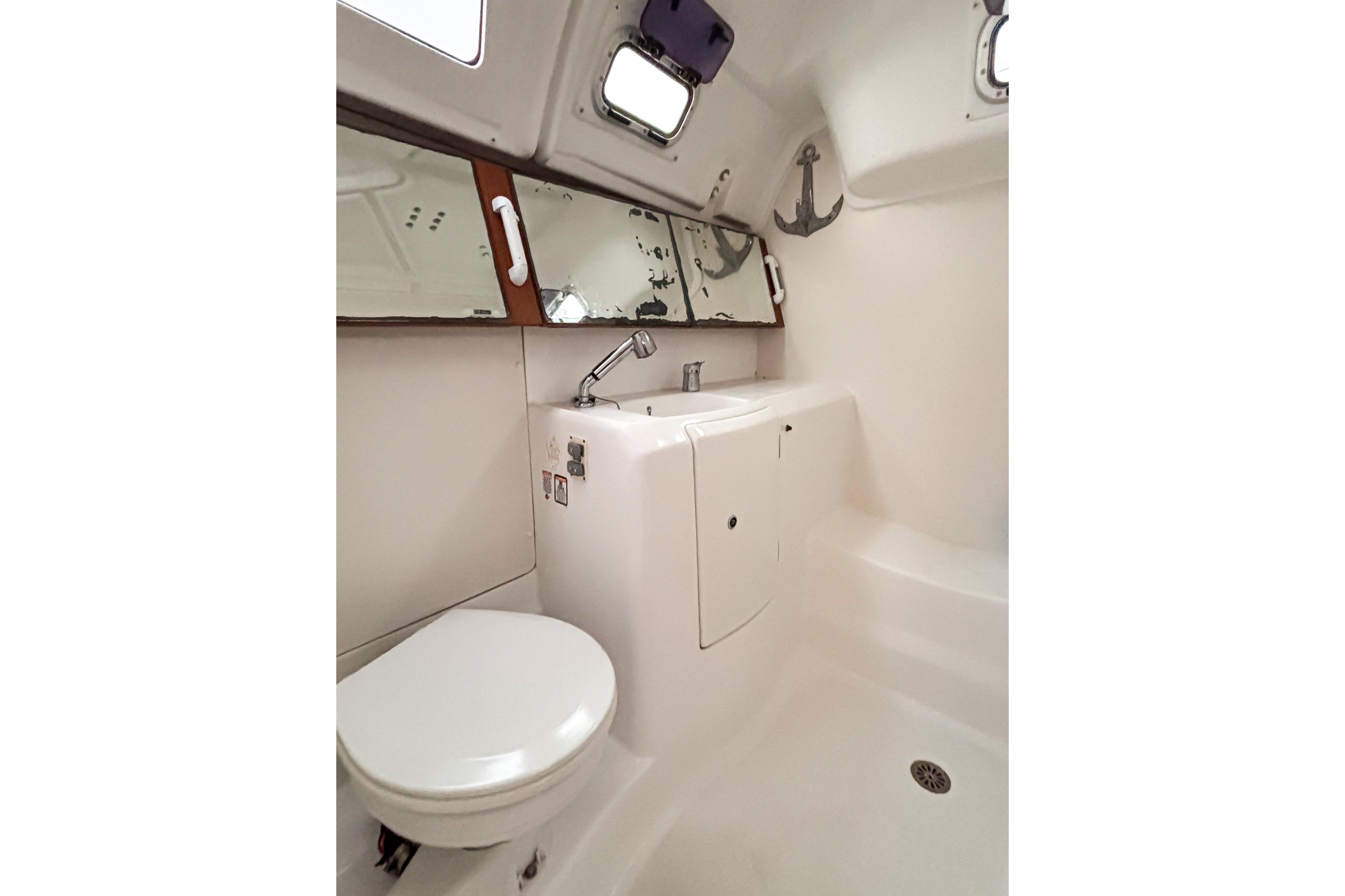Bathroom interior of 2015 Beneteau Oceanis 37 yacht, featuring toilet, sink, and mirror.