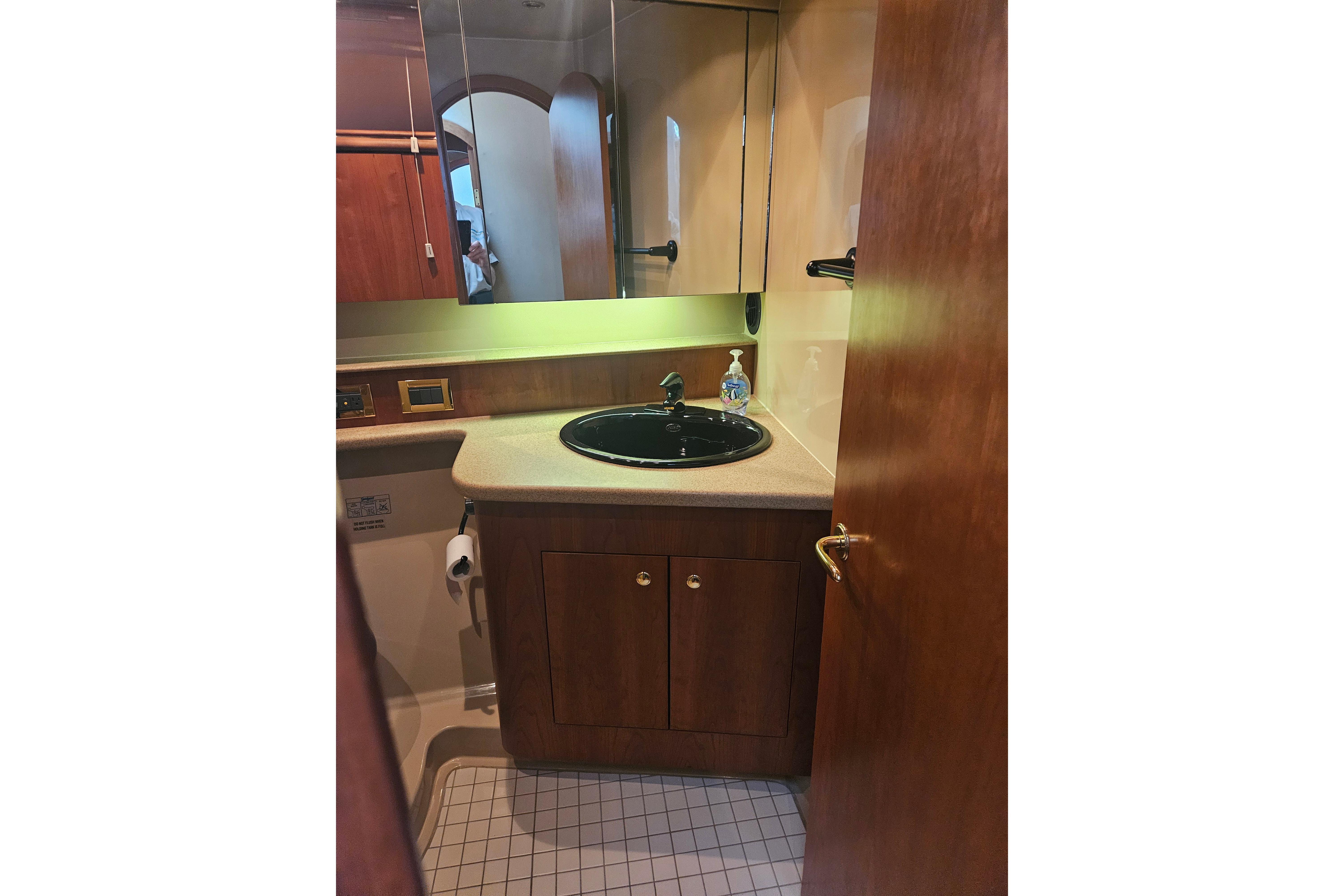 Bathroom interior of 2000 Cruisers Yachts 4450 Express Motoryacht, featuring wood cabinetry and black sink.