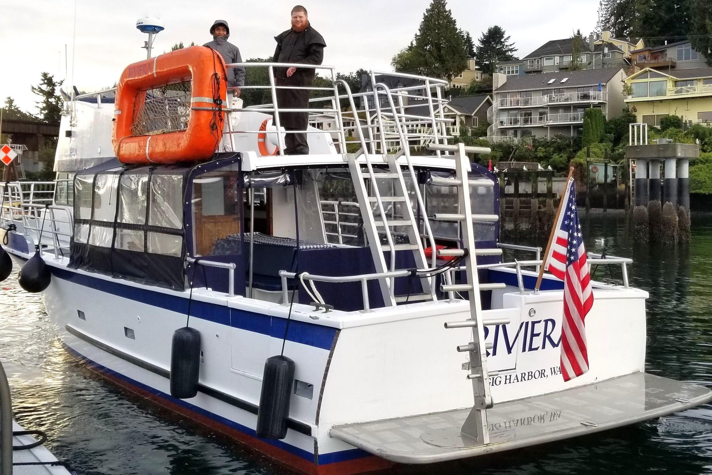 1964 Grandy Tour Boat with American flag docked in scenic harbor setting.