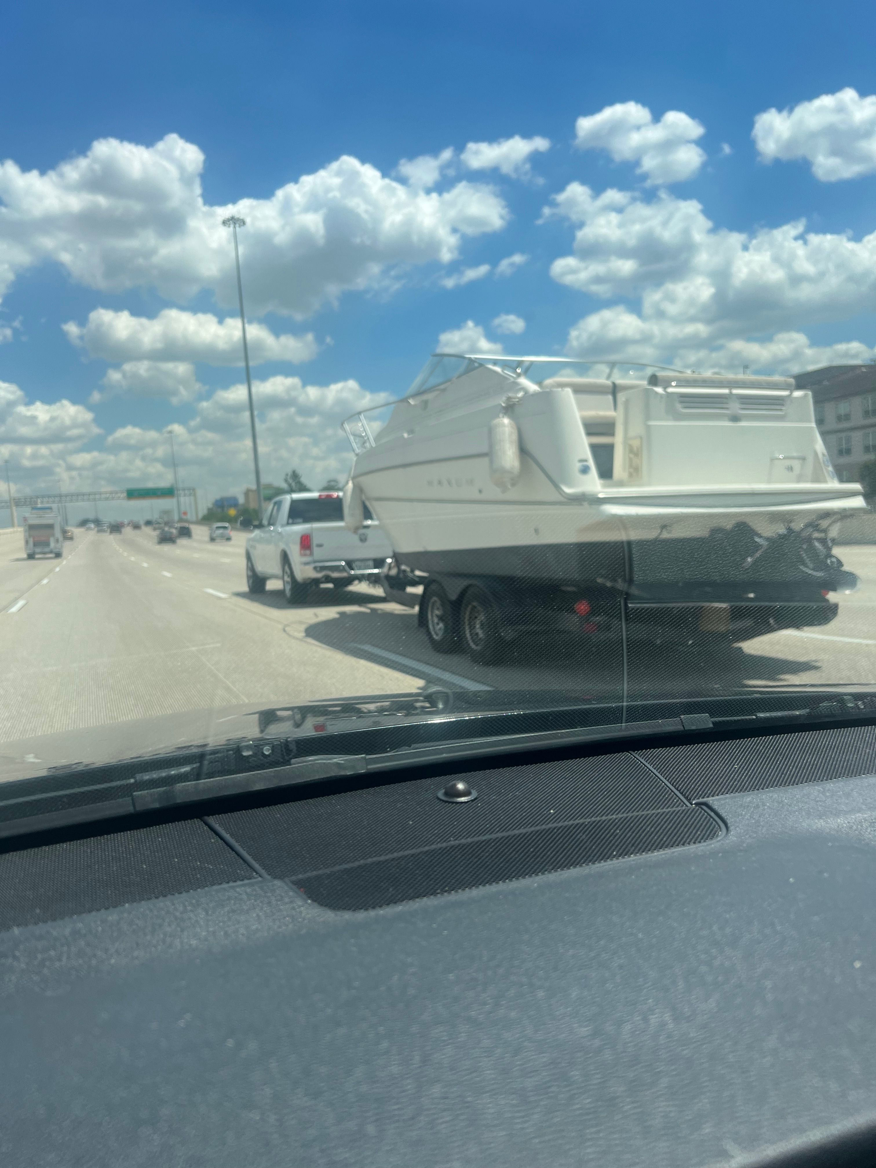 A white boat is being transported on a trailer by a pickup truck on a highway.