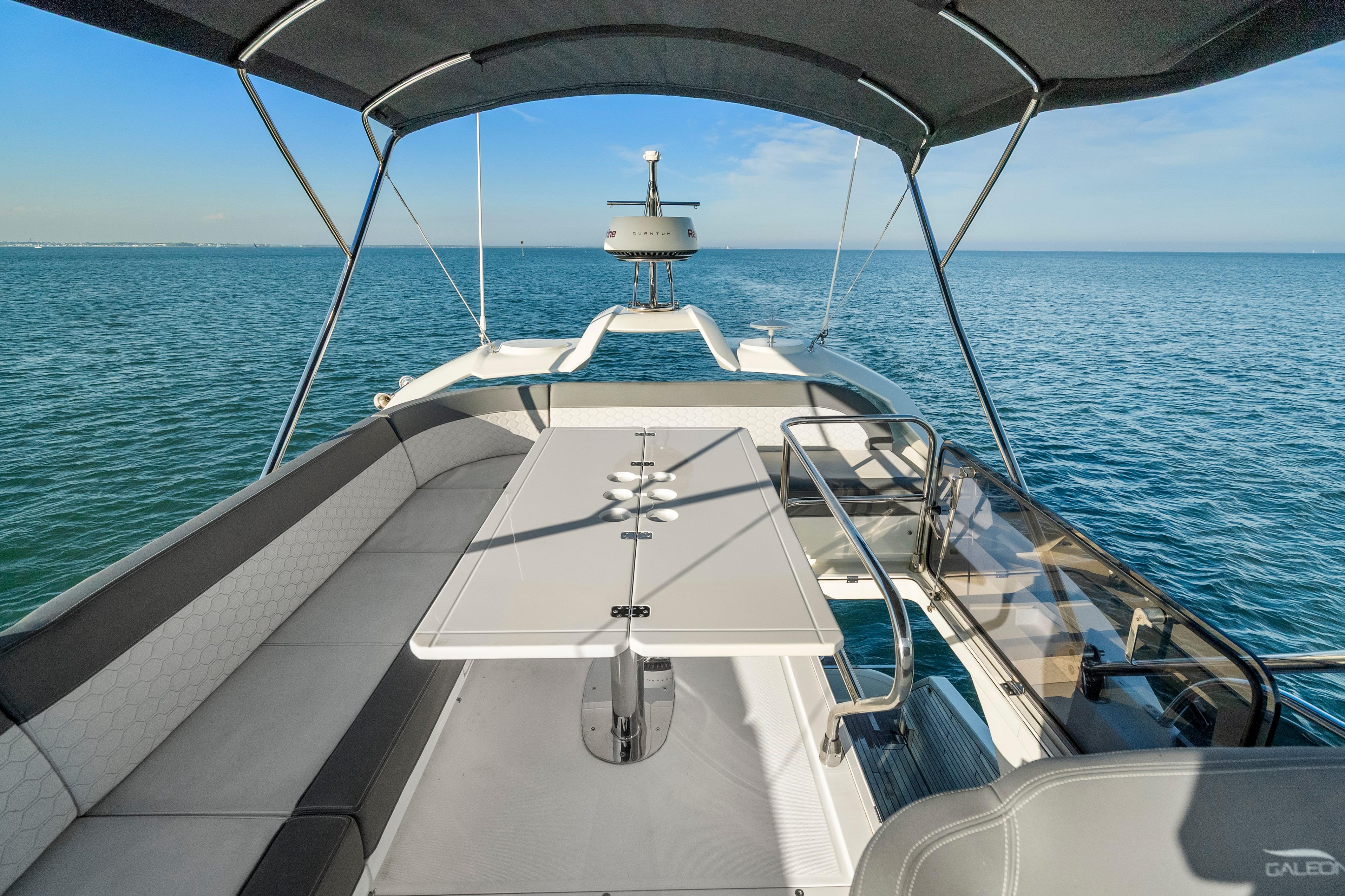 2023 Galeon 400 Fly yacht flybridge with seating and table, overlooking serene ocean waters.