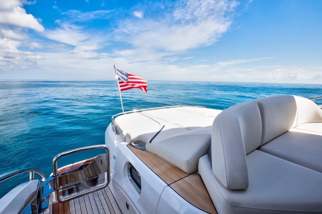 The image shows the stern of a luxury yacht with white cushions and an American flag.