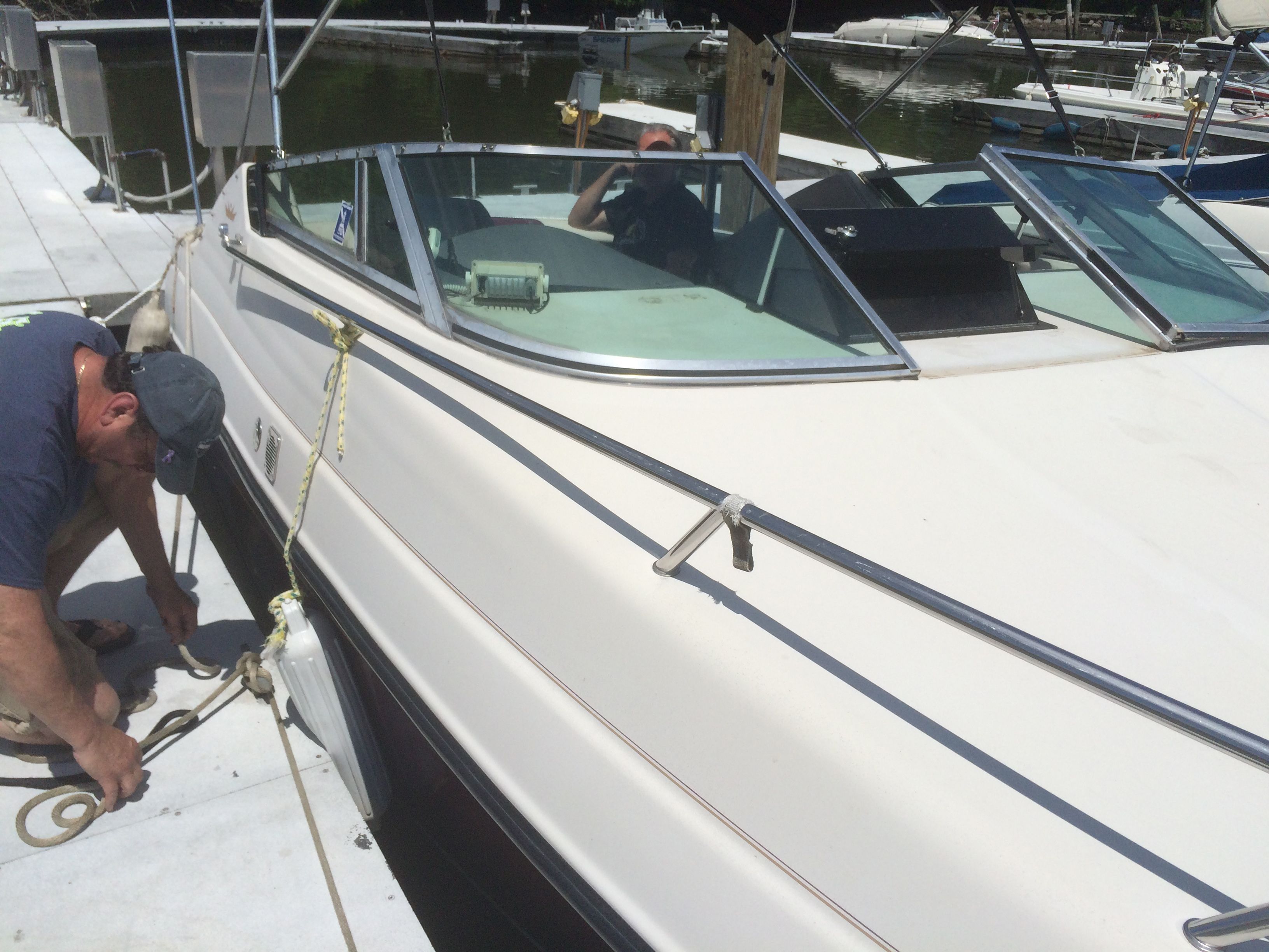 A man secures a boat at the dock. It's a white boat with black accents.