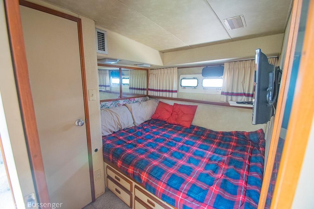 Cozy bedroom interior of 1986 Bertram 42 Convertible yacht with plaid bedding.