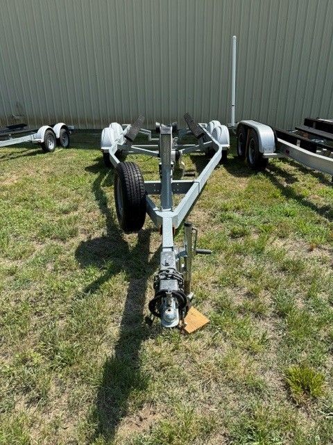 A boat trailer sits on grass in front of a building. It has dual axles and a support wheel.