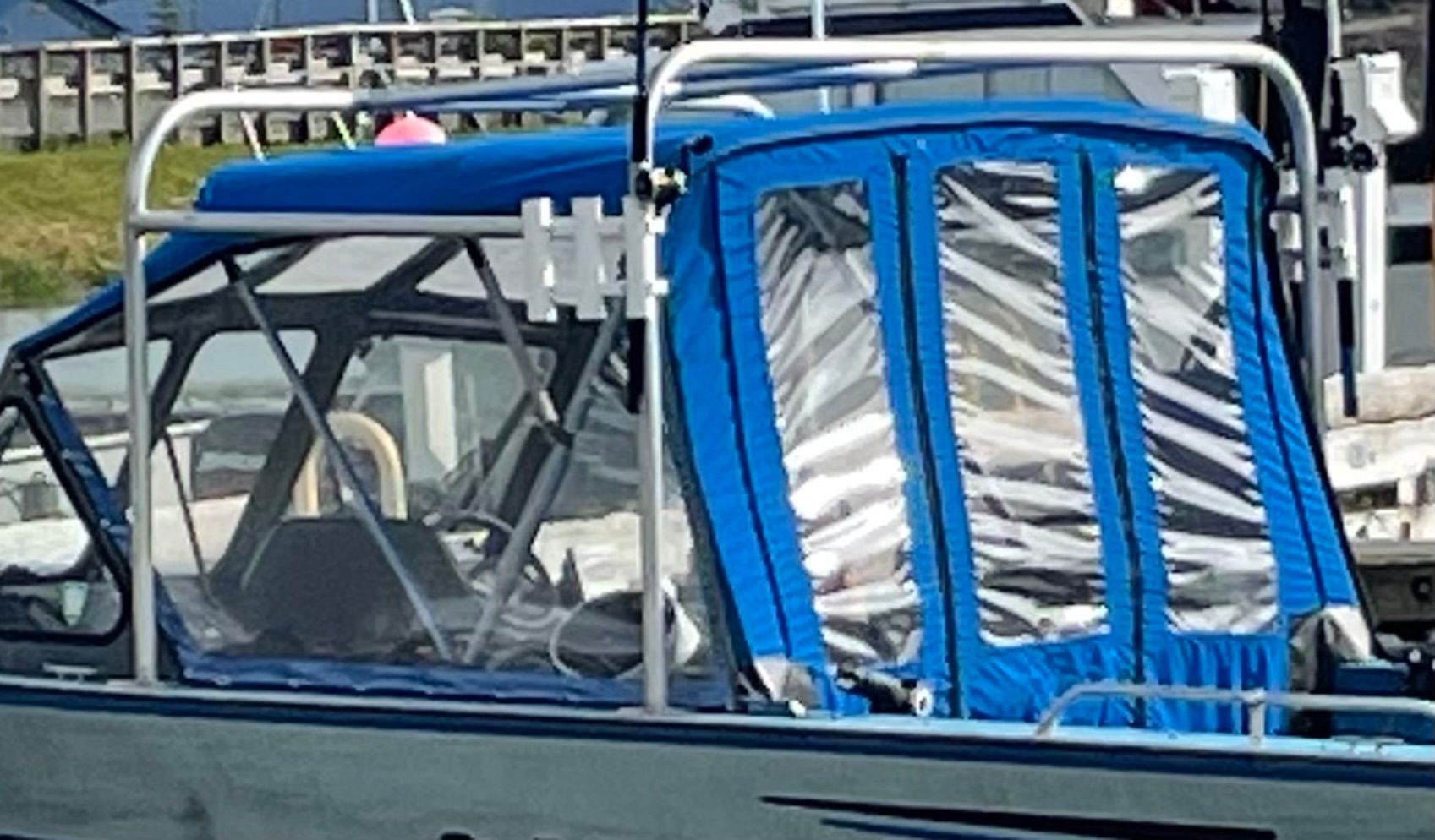 A boat with a blue cover and clear windows is docked at the harbor.