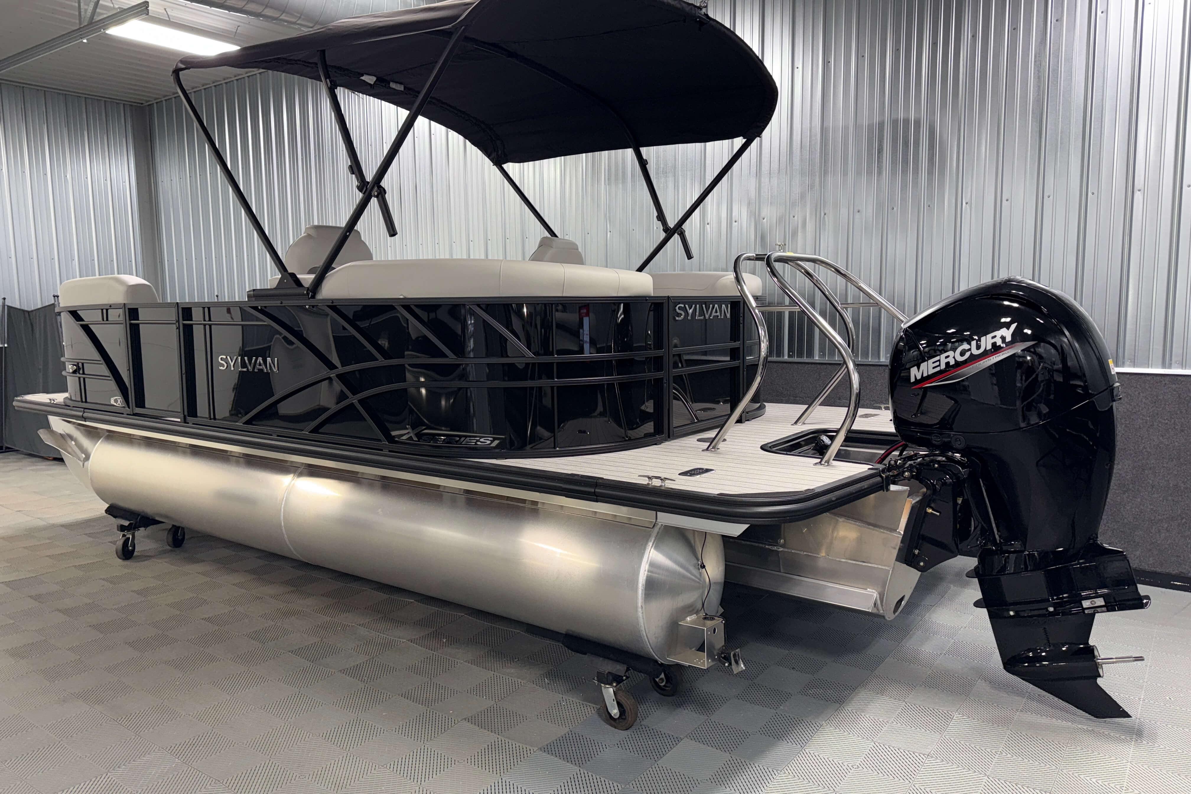 2026 Sylvan Mirage X1 pontoon boat with Mercury outboard motor in a showroom.
