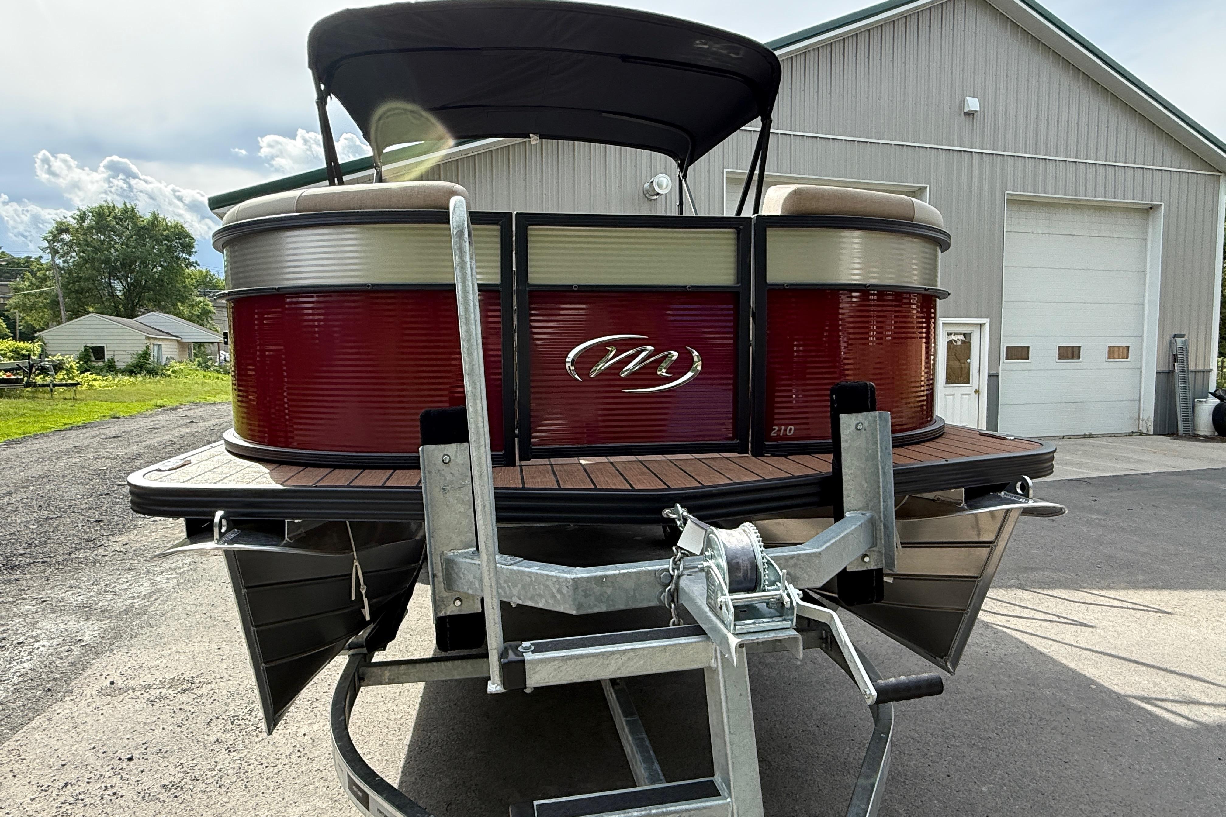 2027 Manitou 21 Aurora LE pontoon boat on trailer, parked outside a garage.