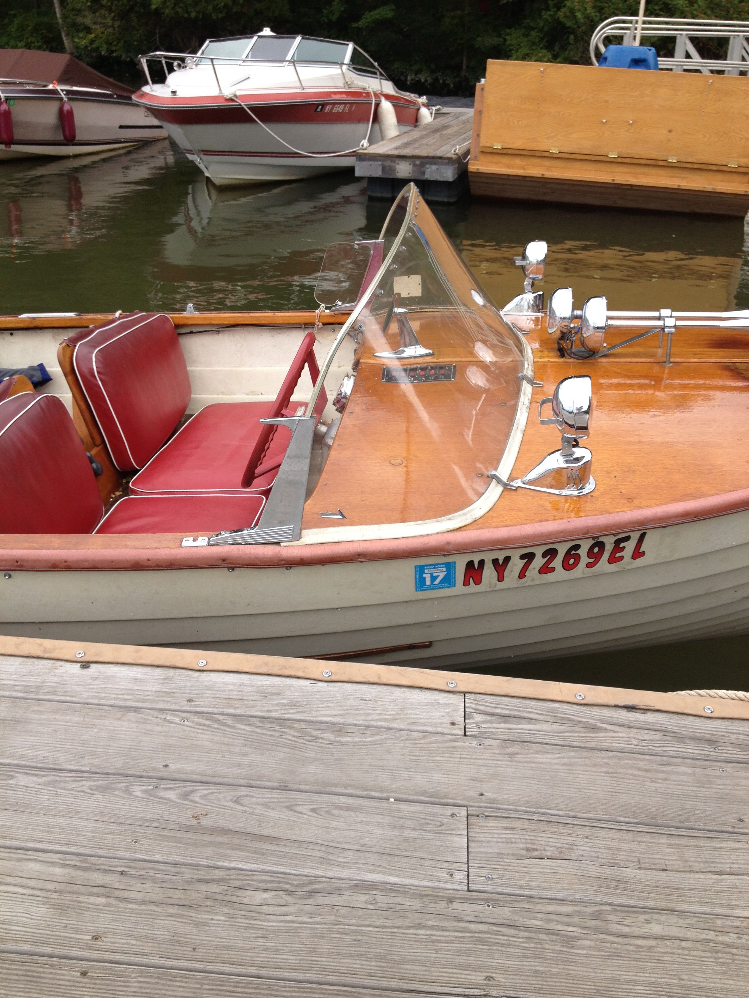 A classic wooden motorboat with red seats and a windshield, docked at a pier.