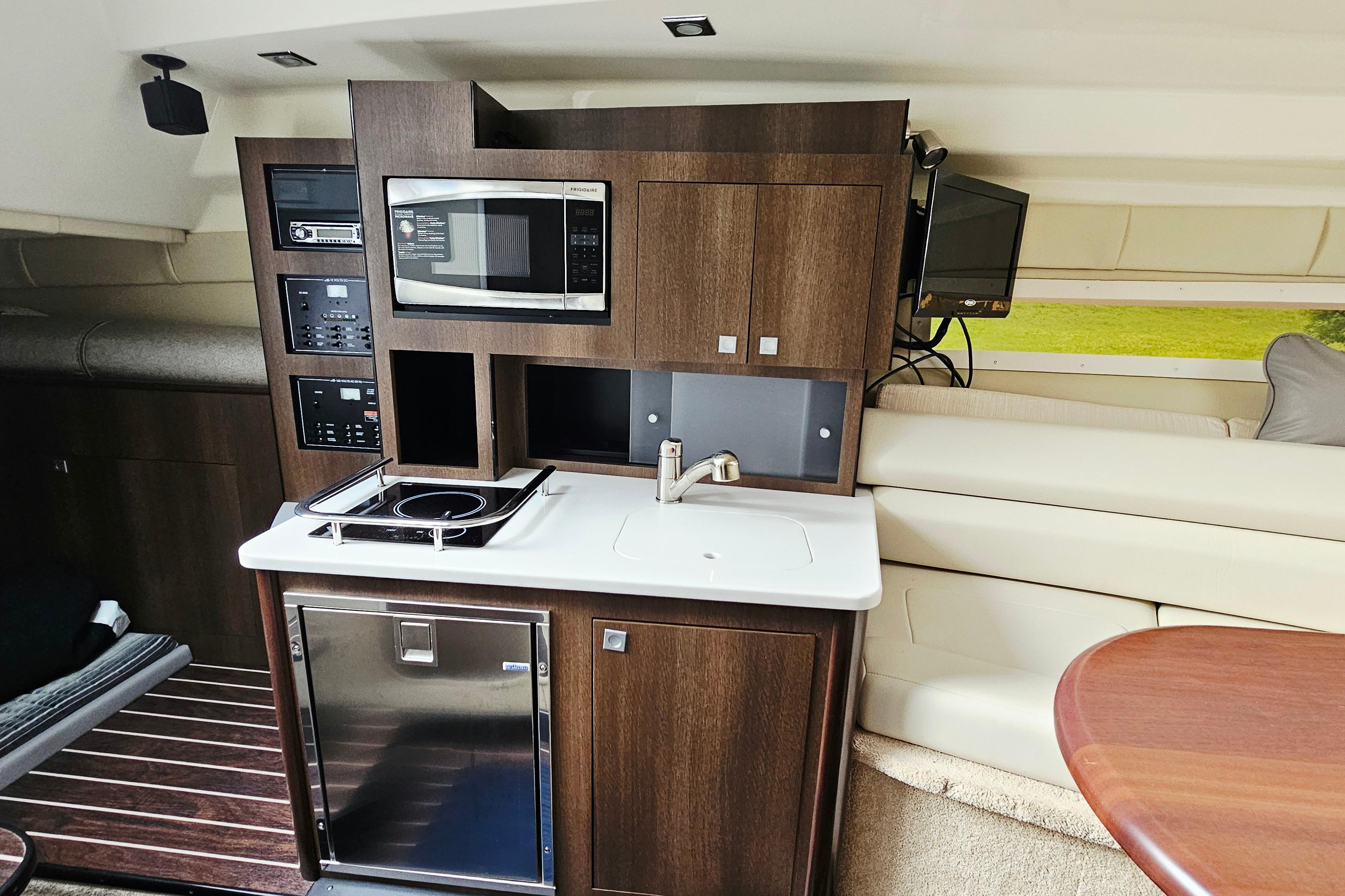Interior of 2016 Monterey 295 Sport Yacht featuring kitchenette with microwave, stove, and sink.