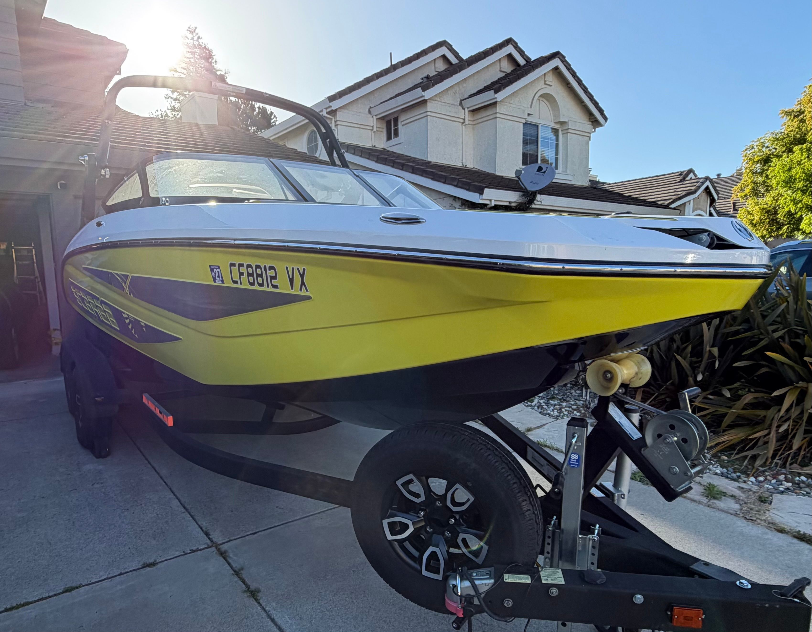 A yellow 2023 Scarab 215 ID boat on a trailer in a driveway.