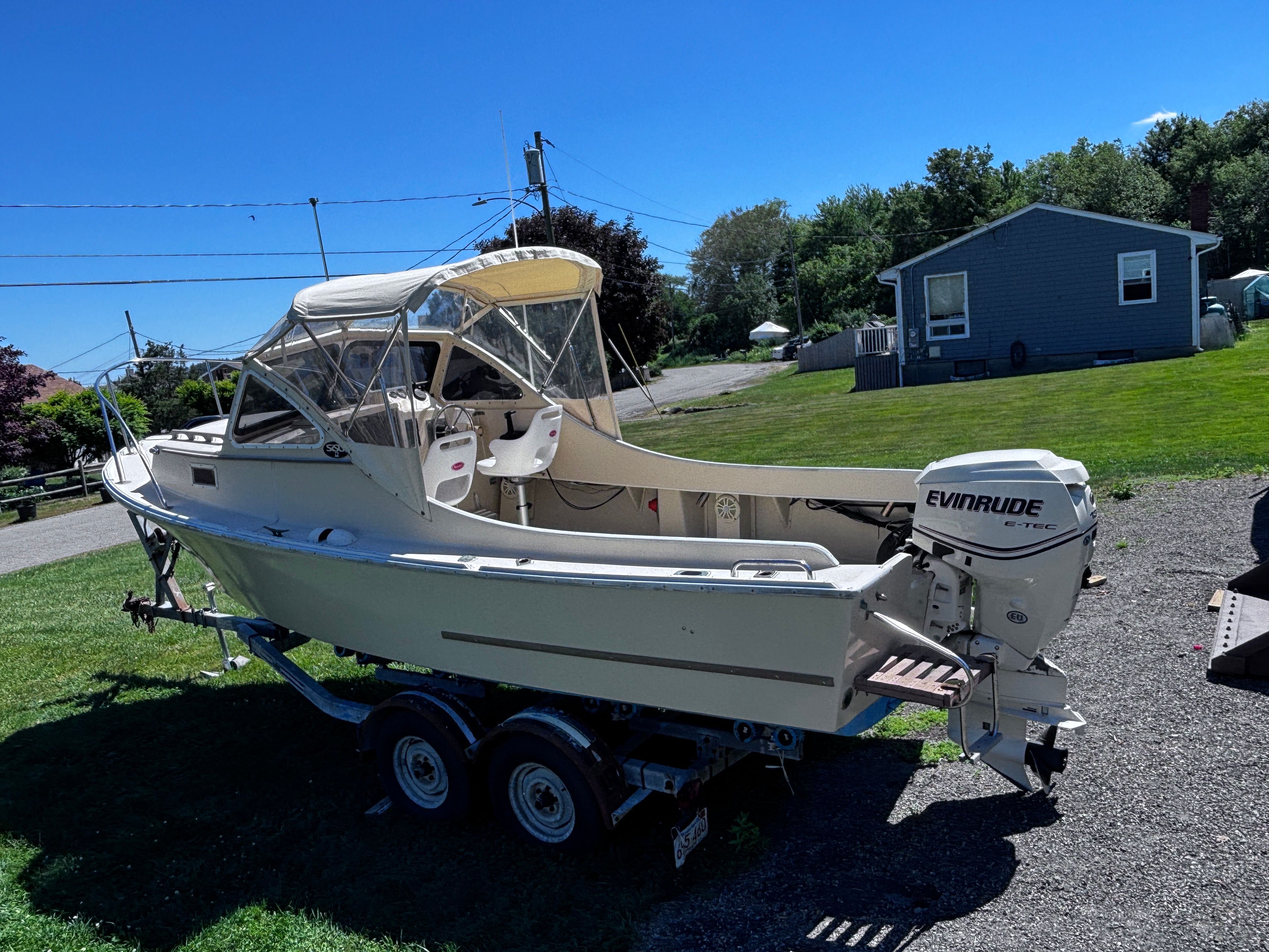 A 1984 SISU 22’ Bass boat on a trailer, with Evinrude motor, sits on a lawn.